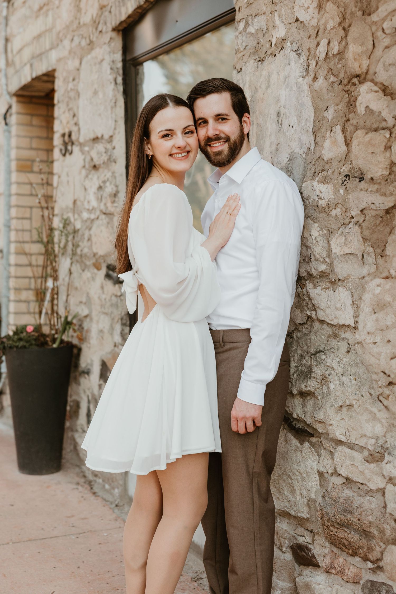 Couple posing romantically against a rustic stone wall during an urban engagement session.