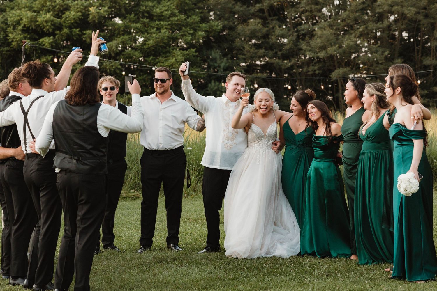 Wedding party celebrating outdoors with bridesmaids in emerald green dresses.