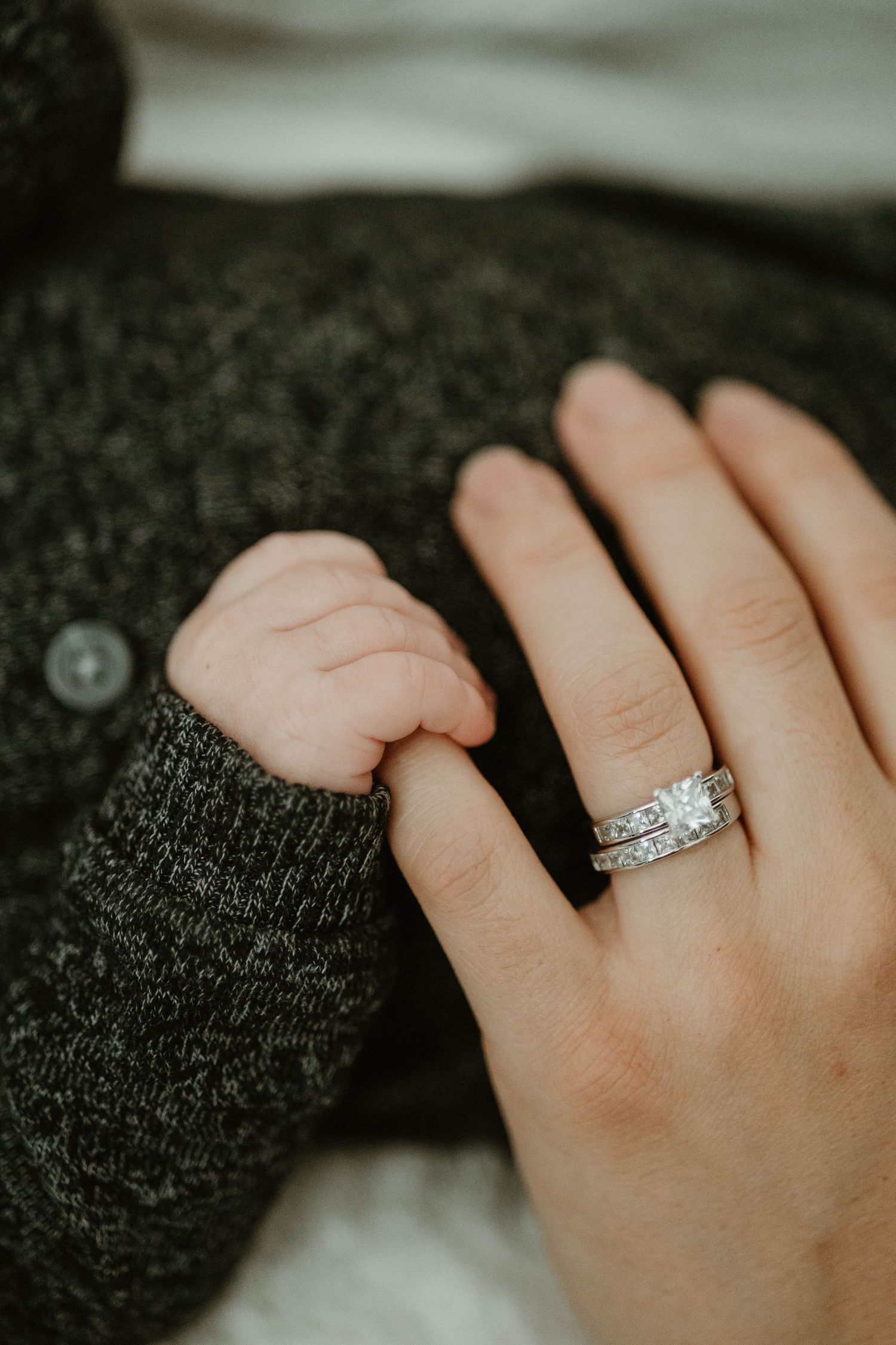 Close-up of a newborn baby's tiny hand gripping a mother's finger adorned with a diamond wedding ring set.