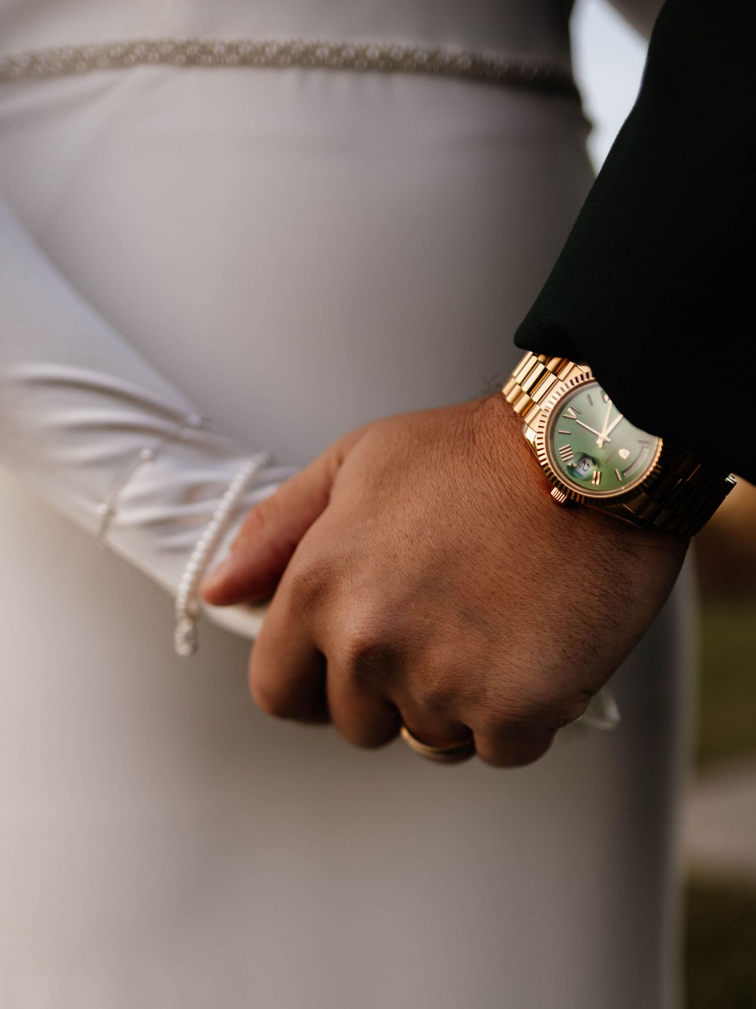 Close-up of groom holding bride's hand wearing a gold Rolex watch with green dial on wedding day.