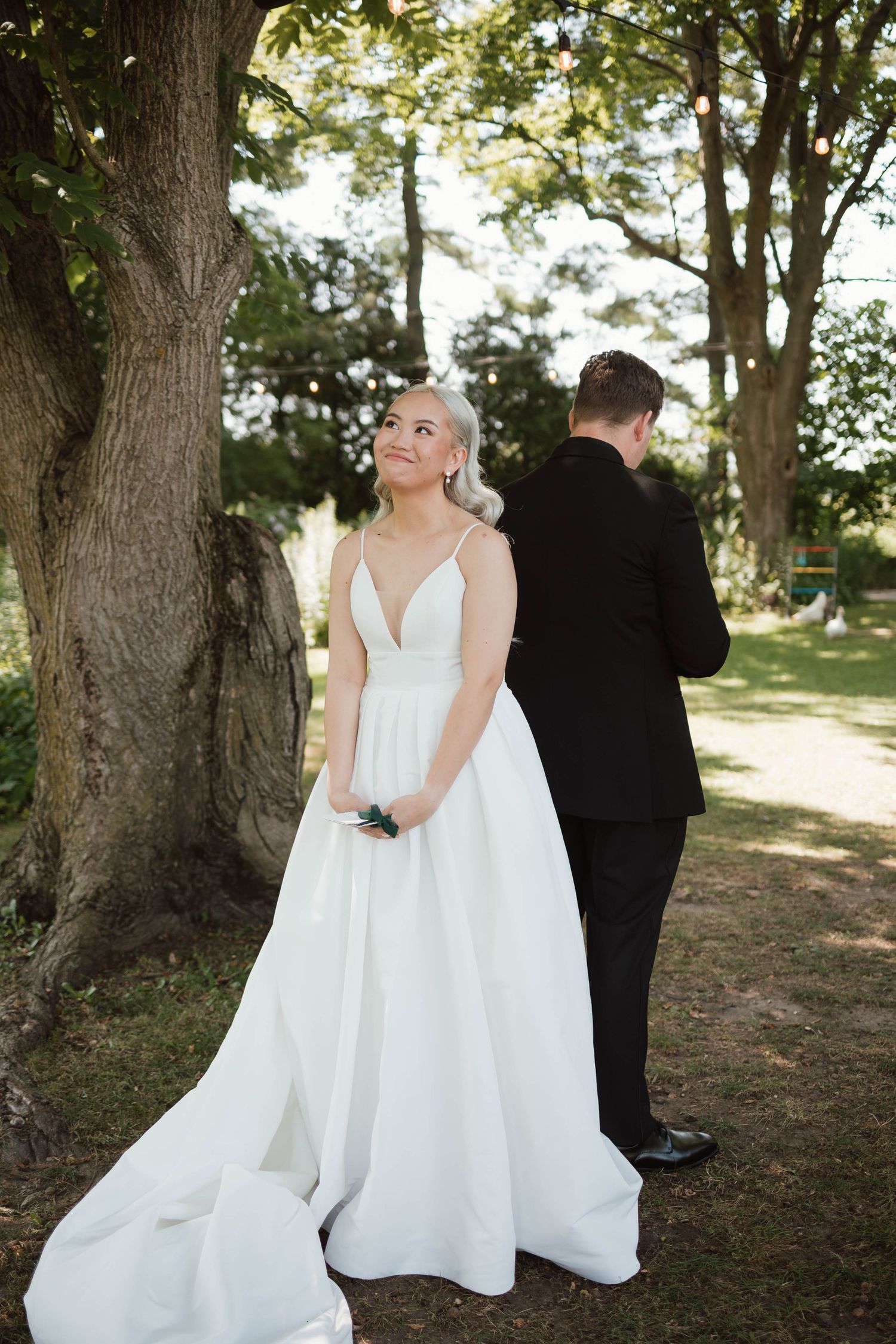 Bride in elegant white ball gown smiling outdoors during first look moment.