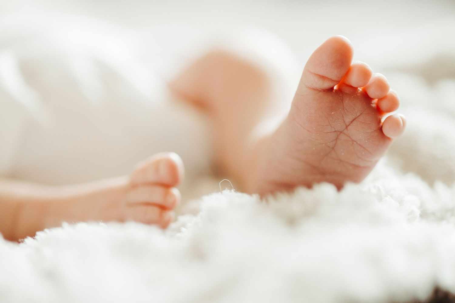 Close-up of tiny newborn baby feet resting on soft white fluffy blanket.