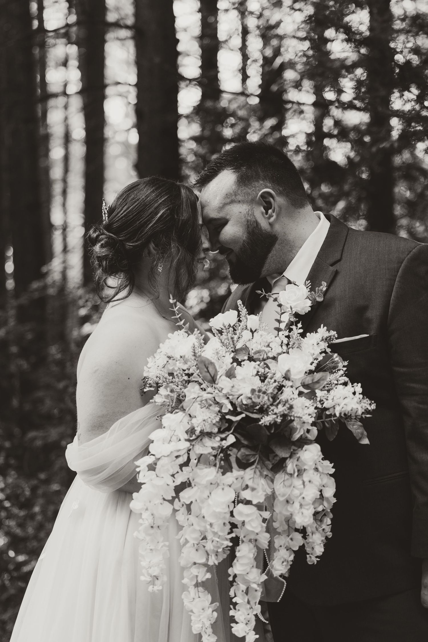 Black and white photo of bride and groom sharing an intimate moment with cascading wedding bouquet.
