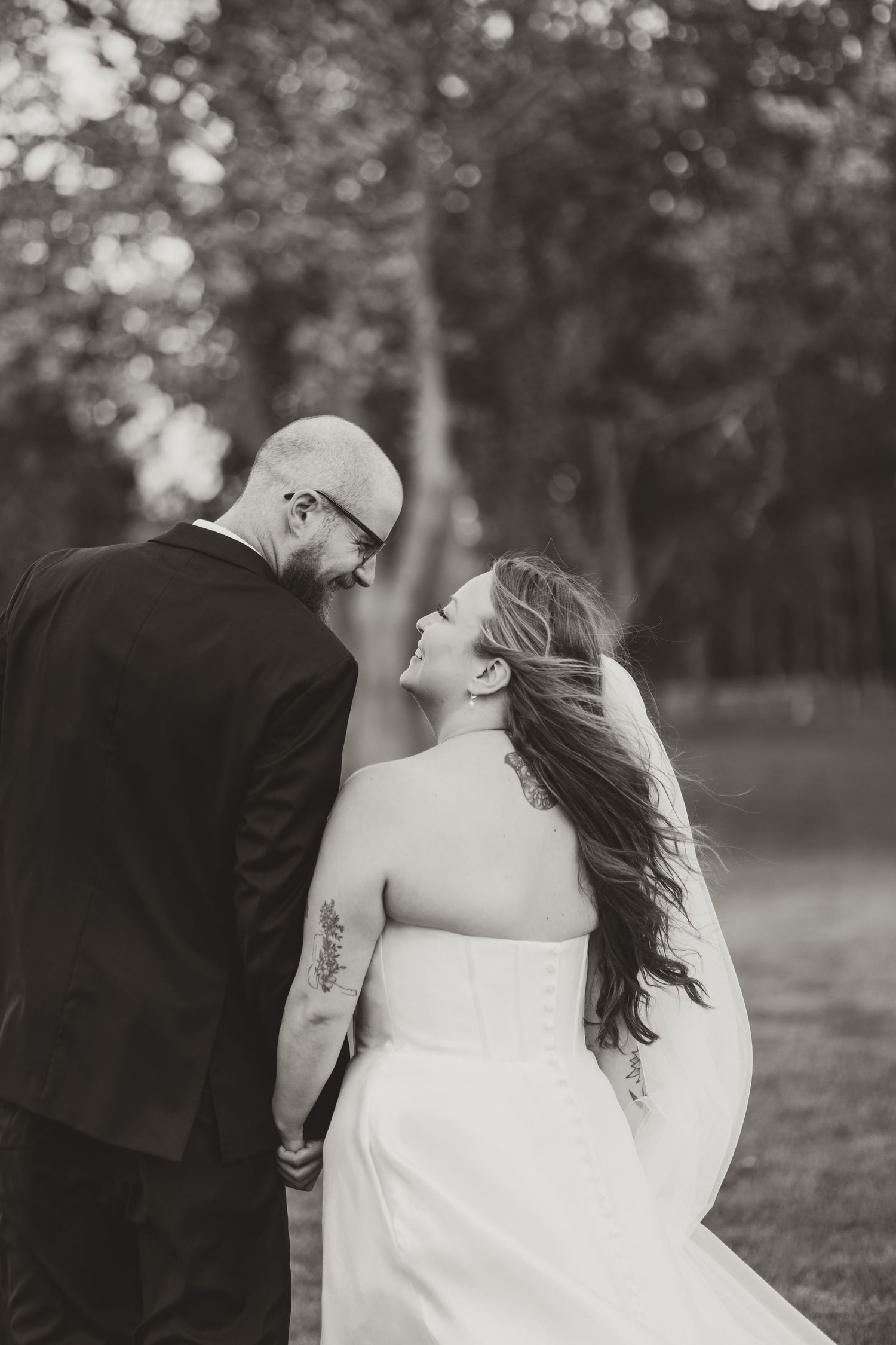 Black and white portrait of bride and groom holding hands and gazing at each other in a garden.