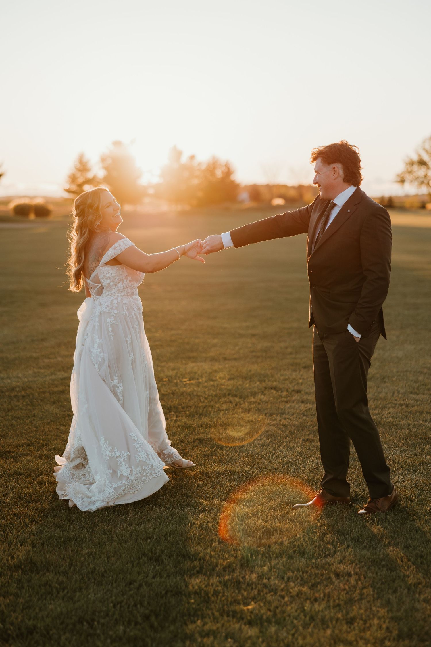 Bride and groom holding hands at sunset on a lush green field during wedding portraits.