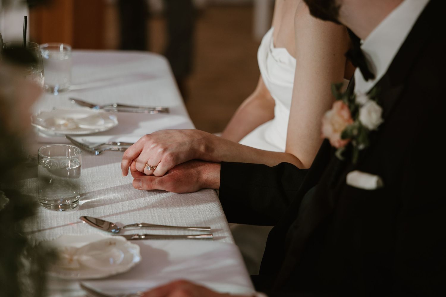 Bride and groom holding hands at the wedding reception dinner table.