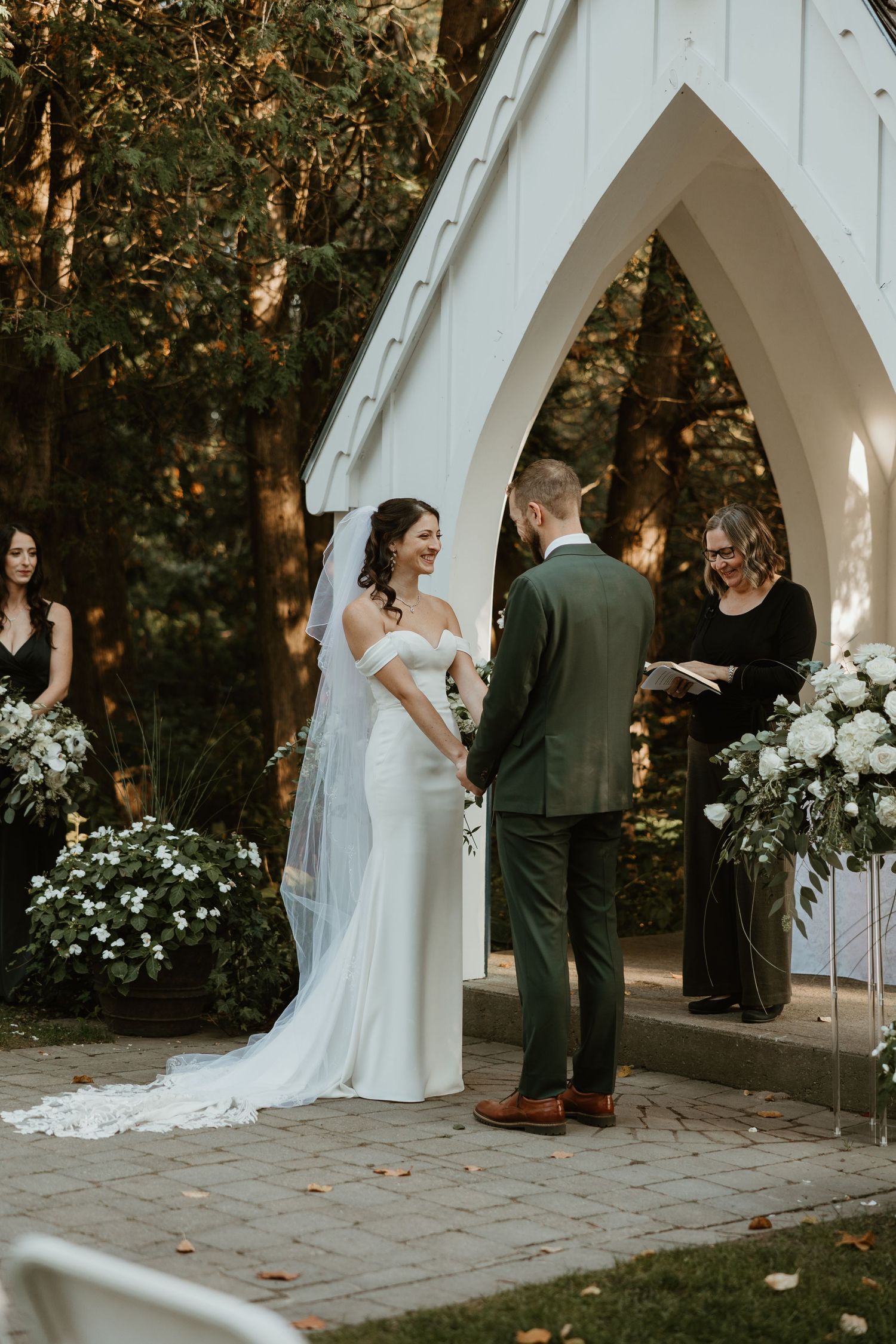 Bride and groom exchange vows at outdoor wedding chapel surrounded by lush greenery.