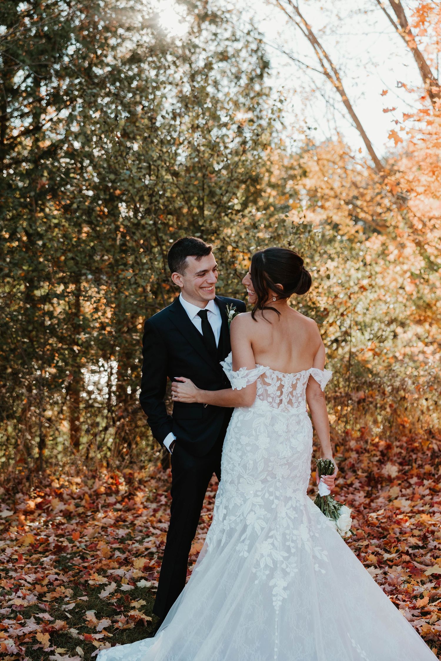 Bride and groom share a romantic moment among autumn foliage, bride in lace off-shoulder gown.