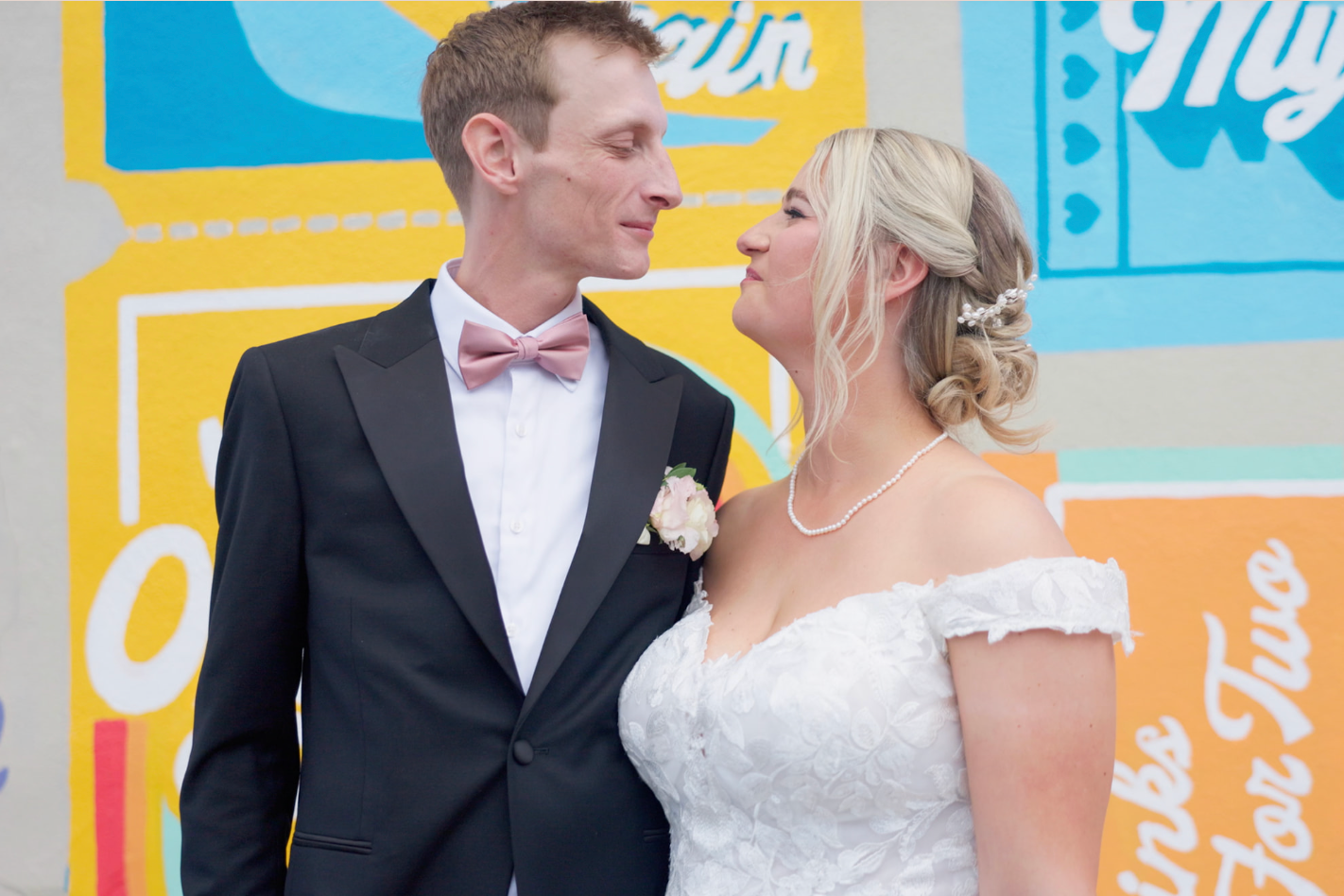 Bride and groom sharing a smile in front of a colorful retro-themed backdrop at their wedding.