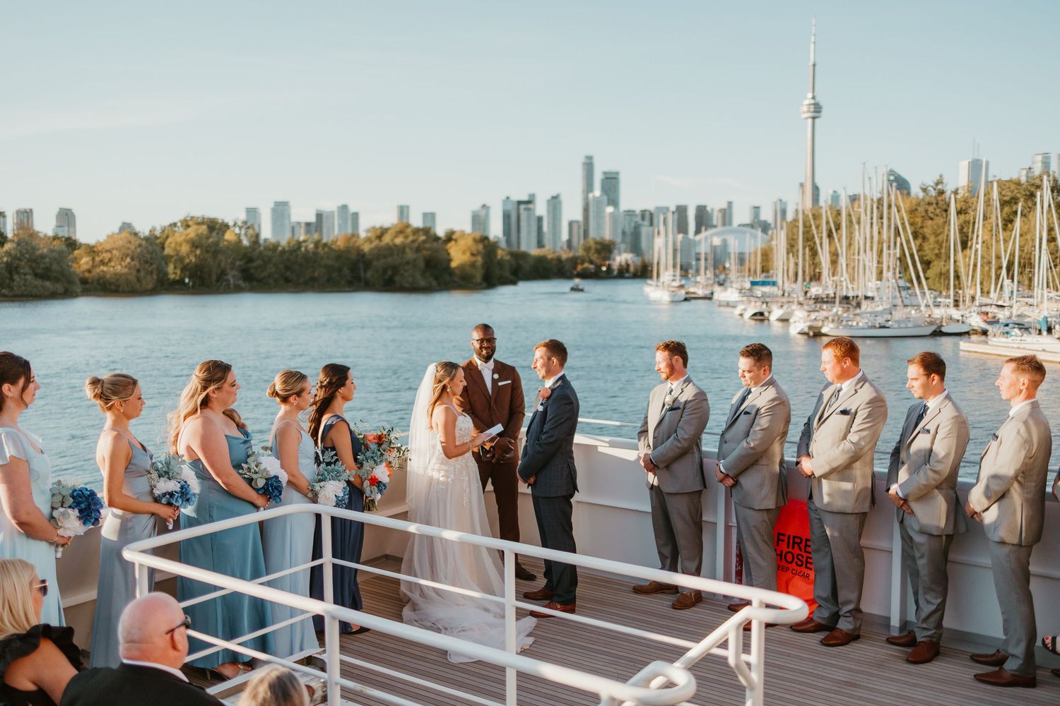 Outdoor wedding ceremony on a waterfront dock with Toronto skyline and CN Tower in the background.