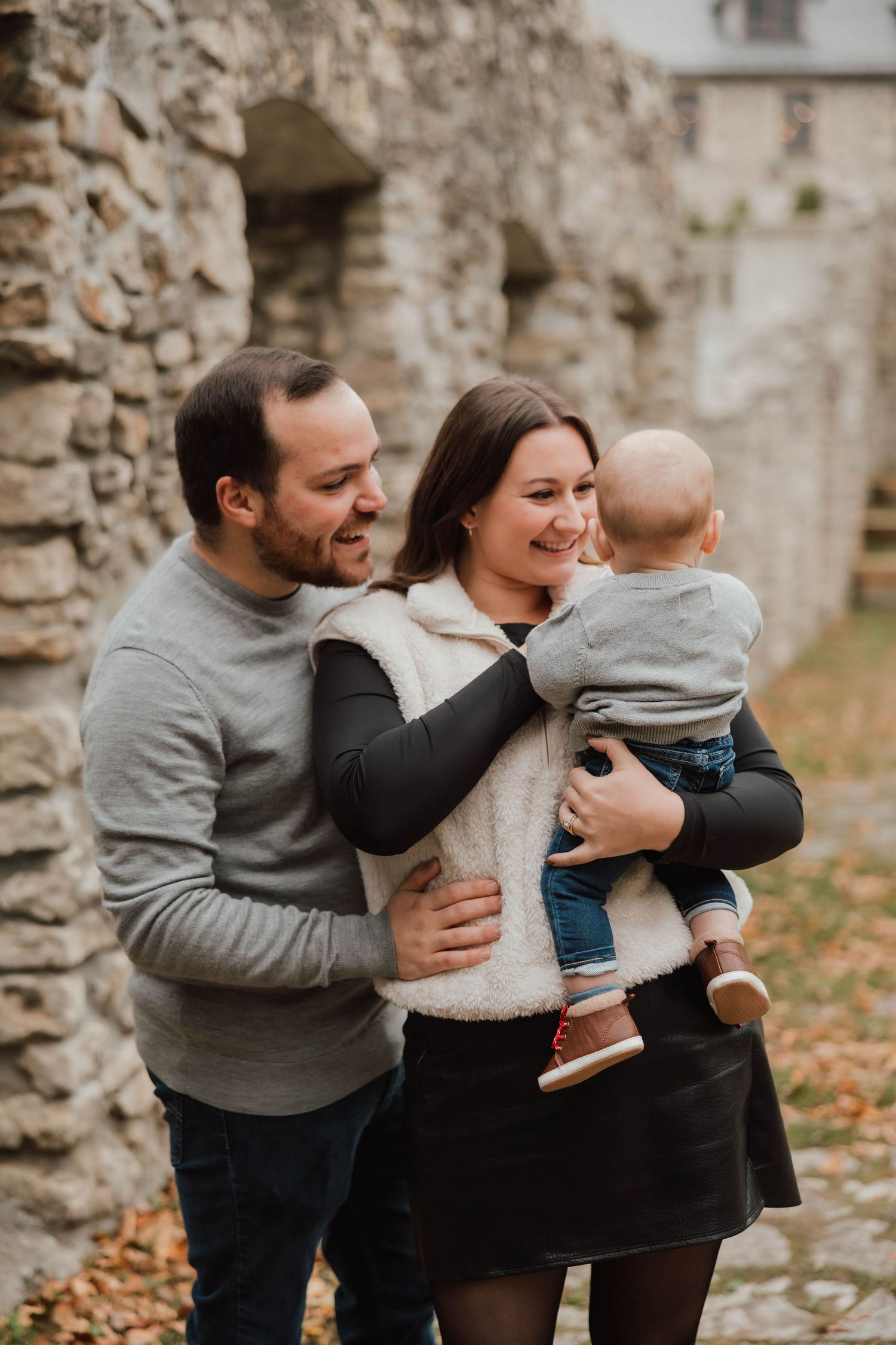 Happy family with parents and baby pose together near rustic stone ruins in autumn setting.