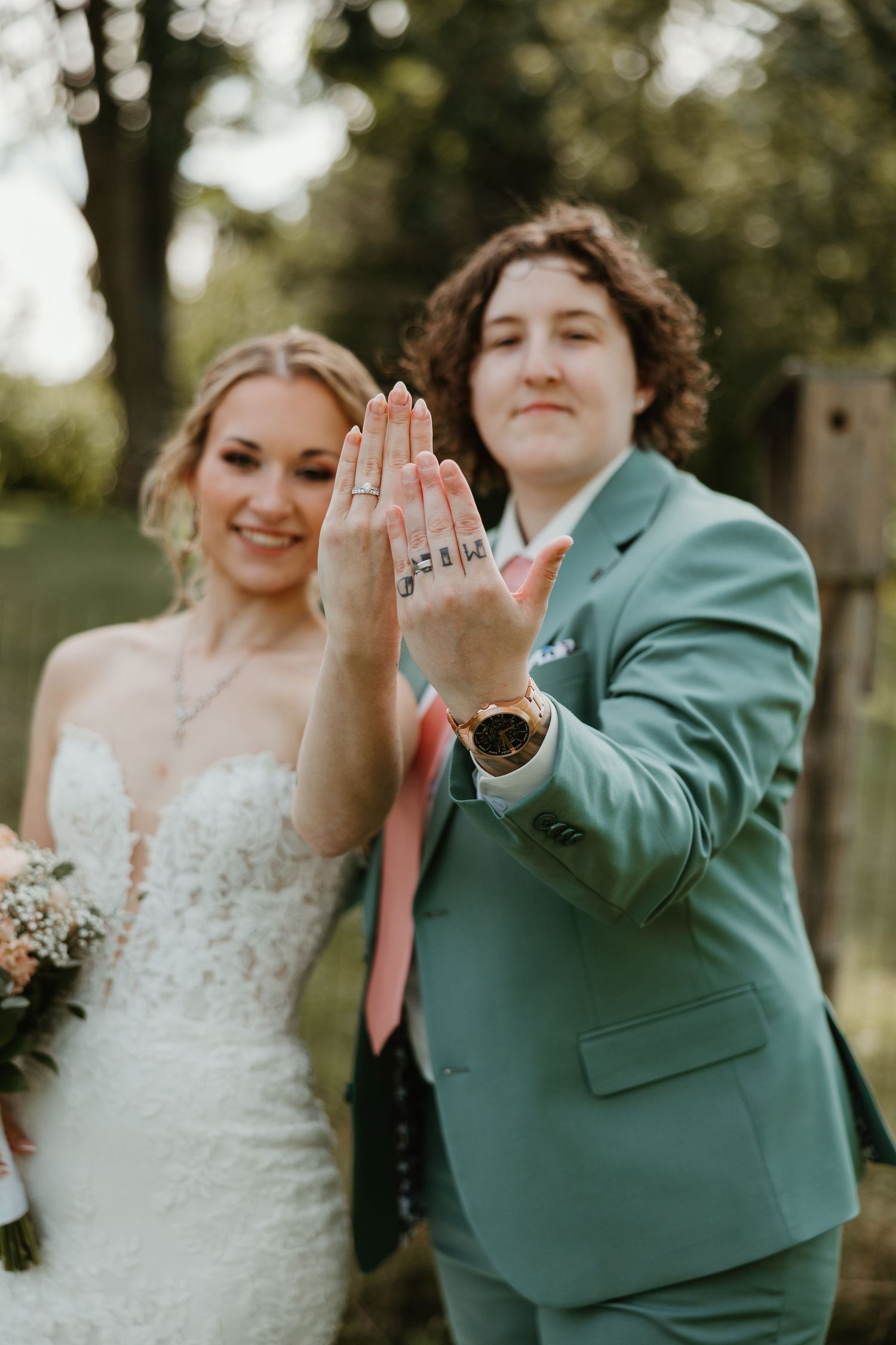 Newlywed couple showing off wedding rings outdoors in green garden setting.