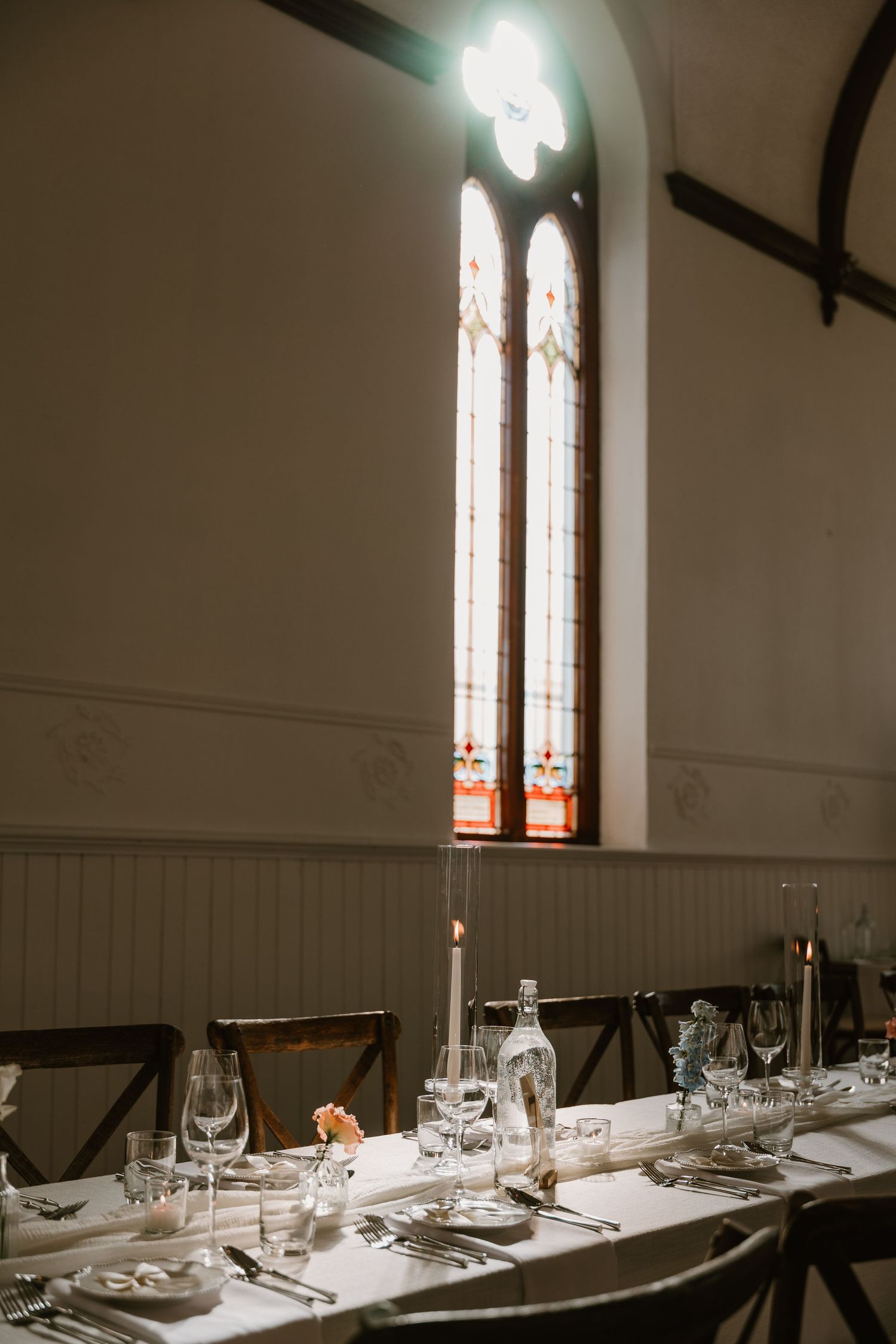 Elegant wedding reception table set beneath a stained glass arched church window.