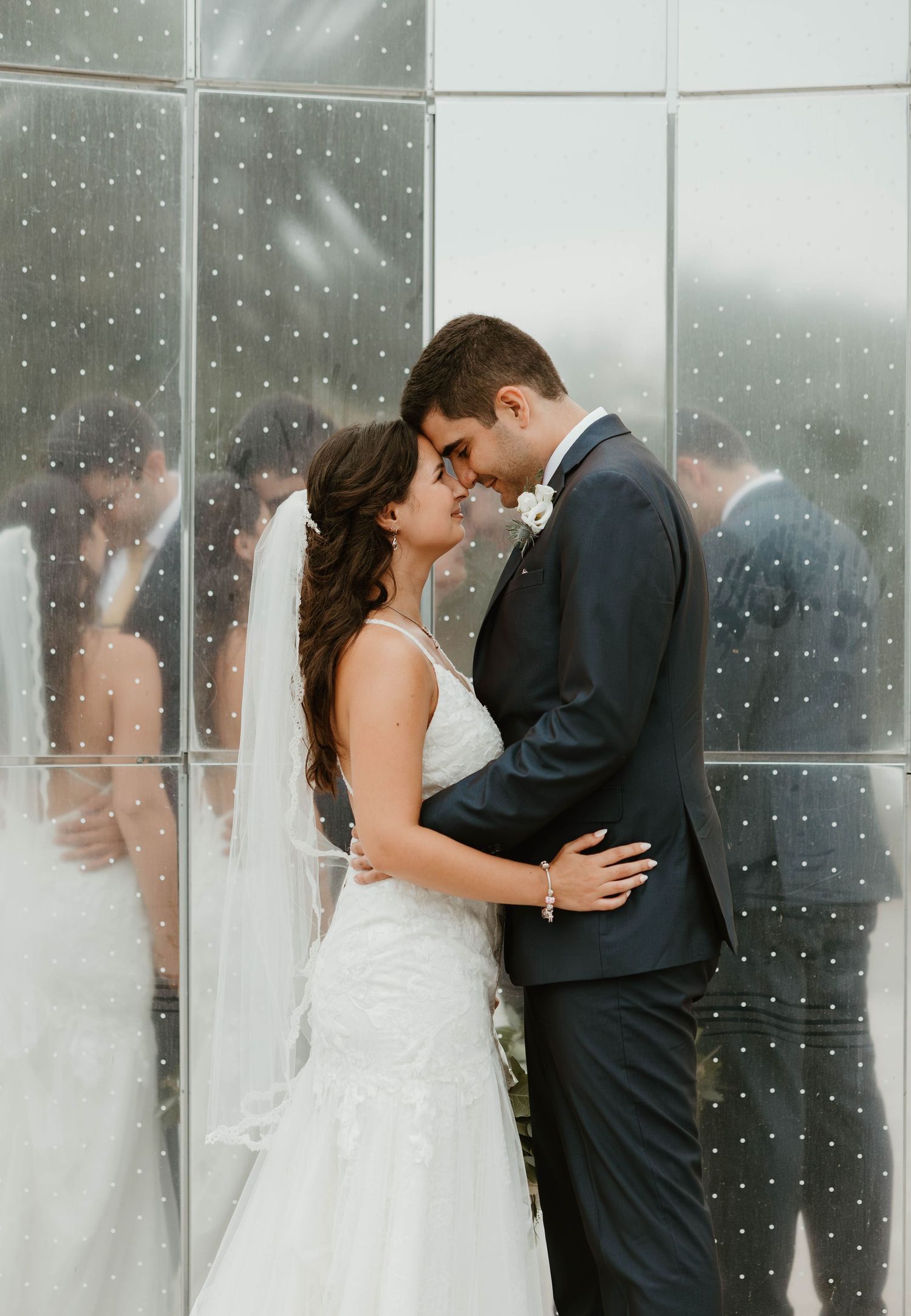 Bride and groom sharing romantic moment against reflective mirrored glass wall.