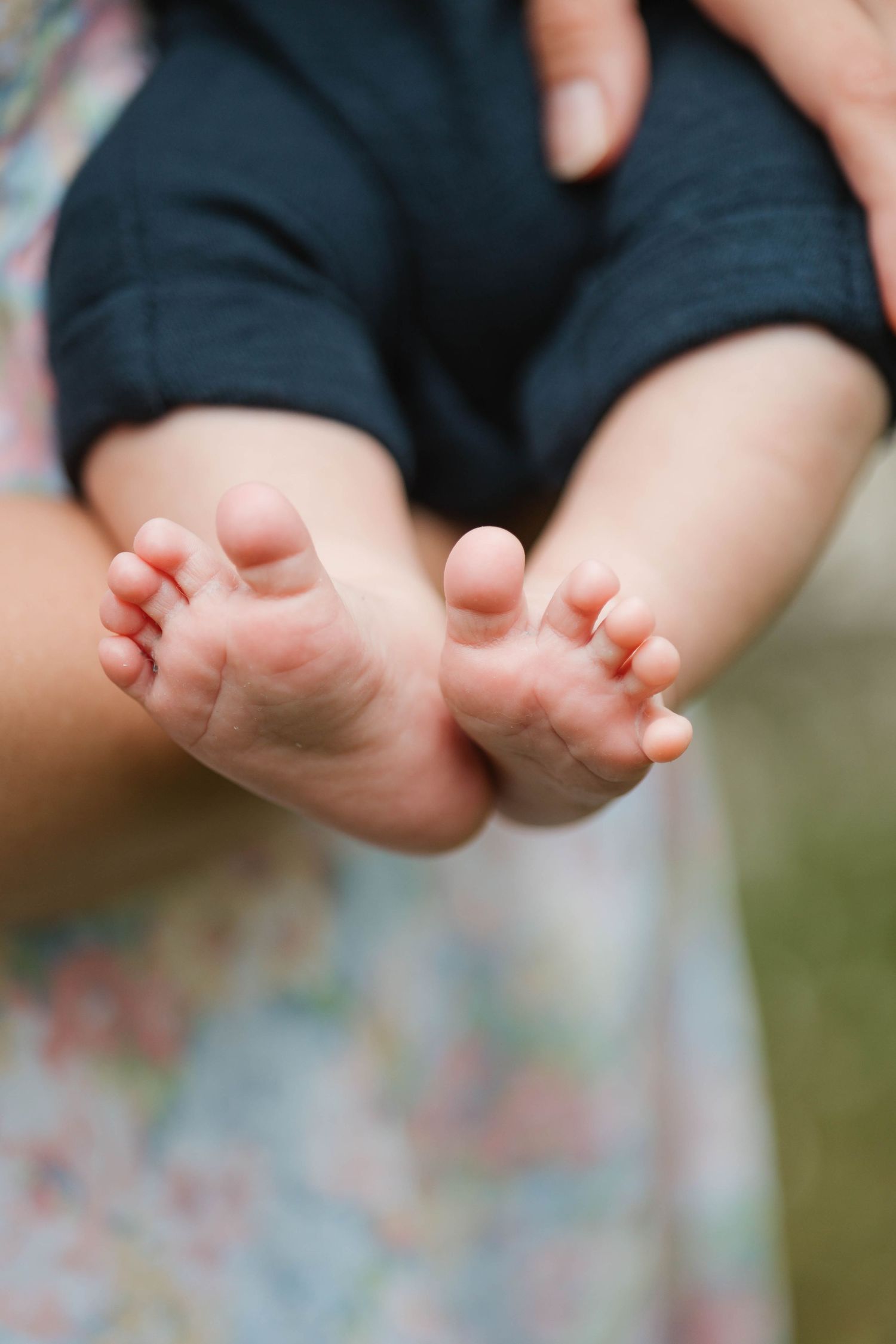 Close-up of tiny newborn baby feet held gently in a mother's hands outdoors.