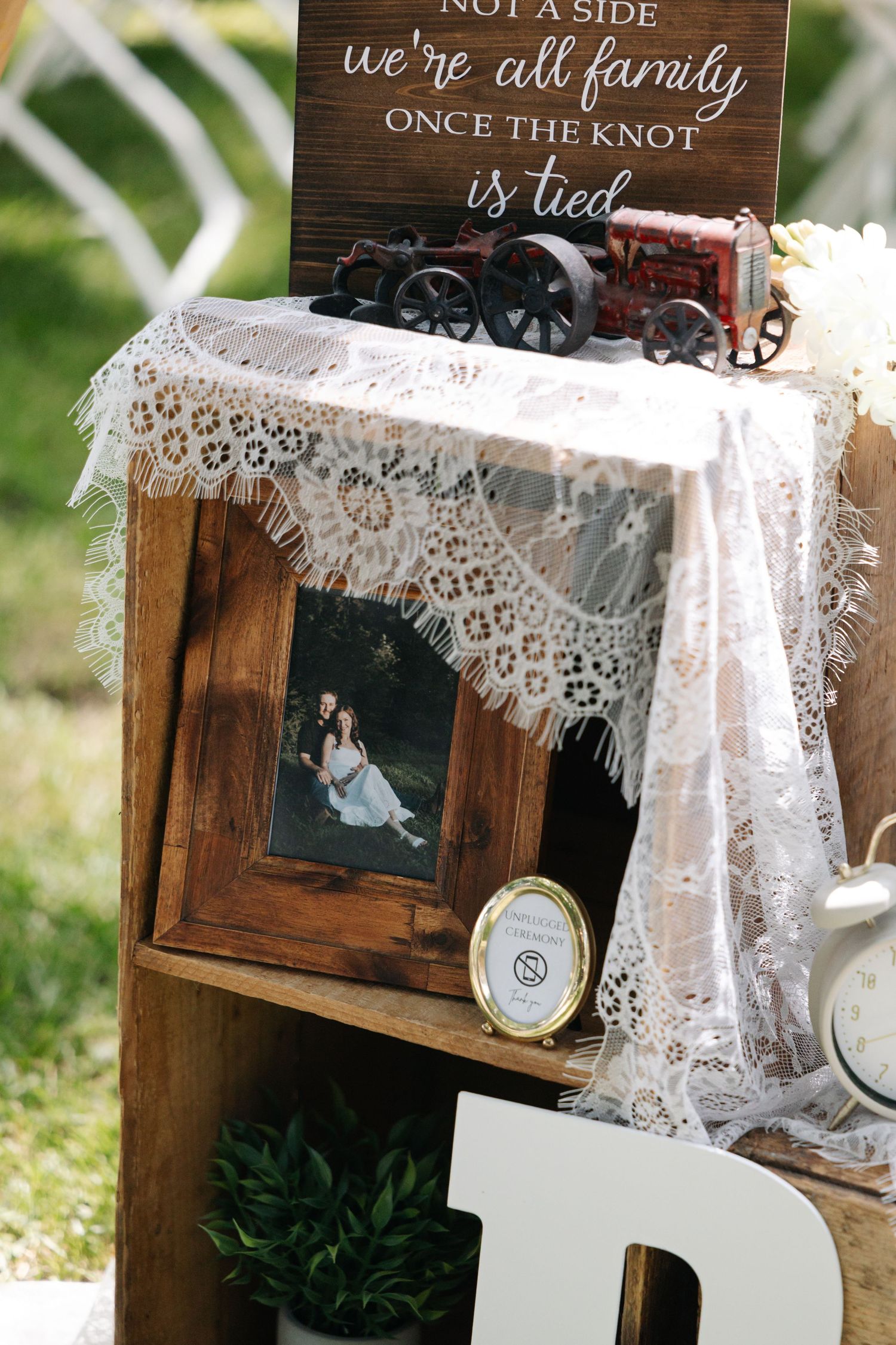 Rustic wedding decor display with wooden crates, lace, framed couple photo, and a sign reading we are all family once the knot is tied.