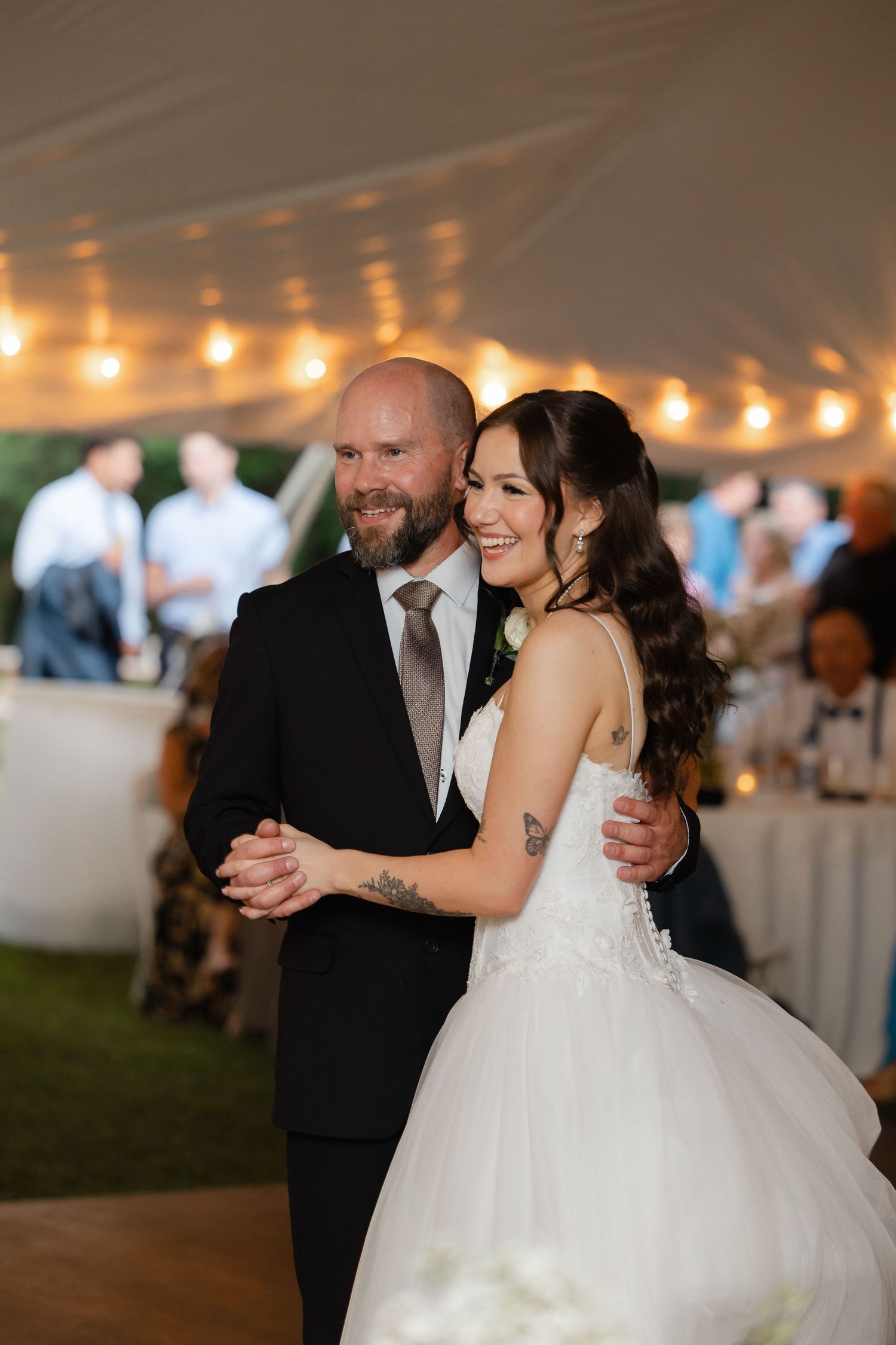 Bride and groom share first dance under string lights at elegant tented wedding reception.