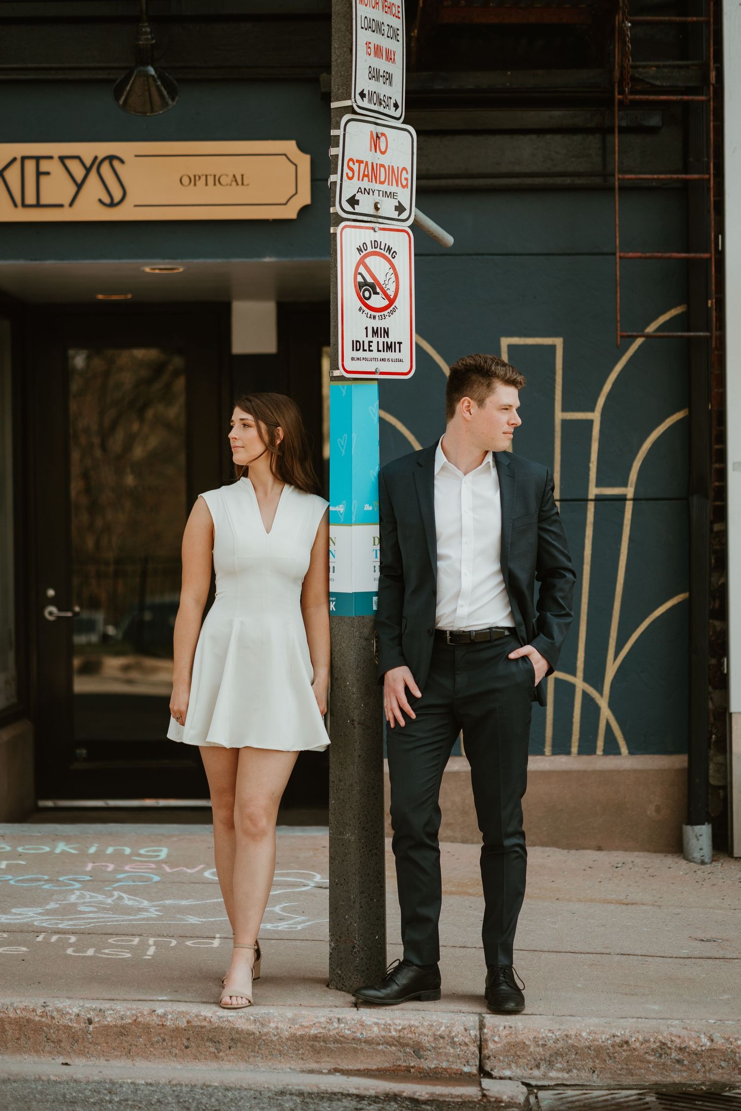 Stylish engaged couple posing separately by a street pole in an urban city setting.