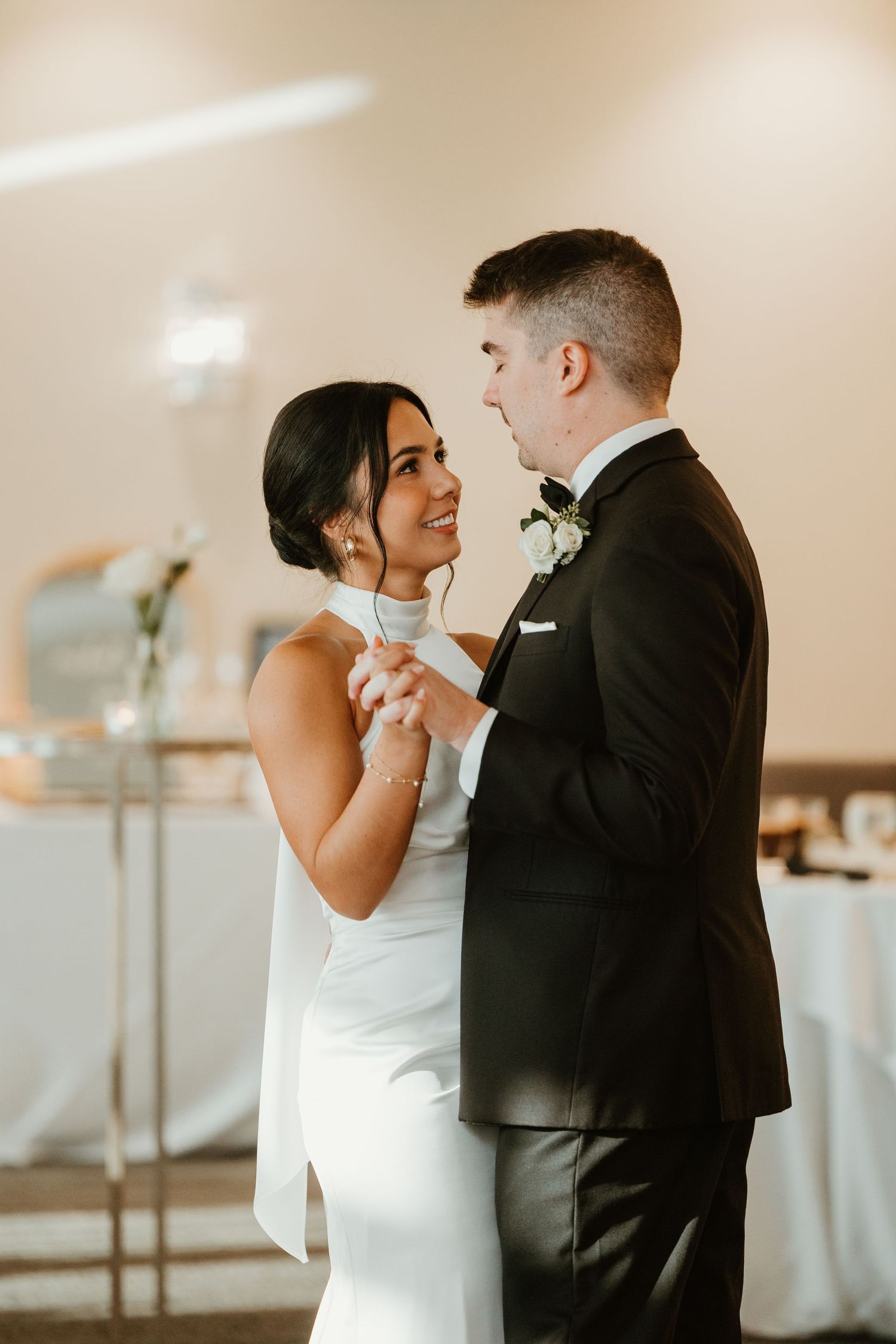 Bride and groom sharing first dance, smiling at each other in elegant wedding reception venue.