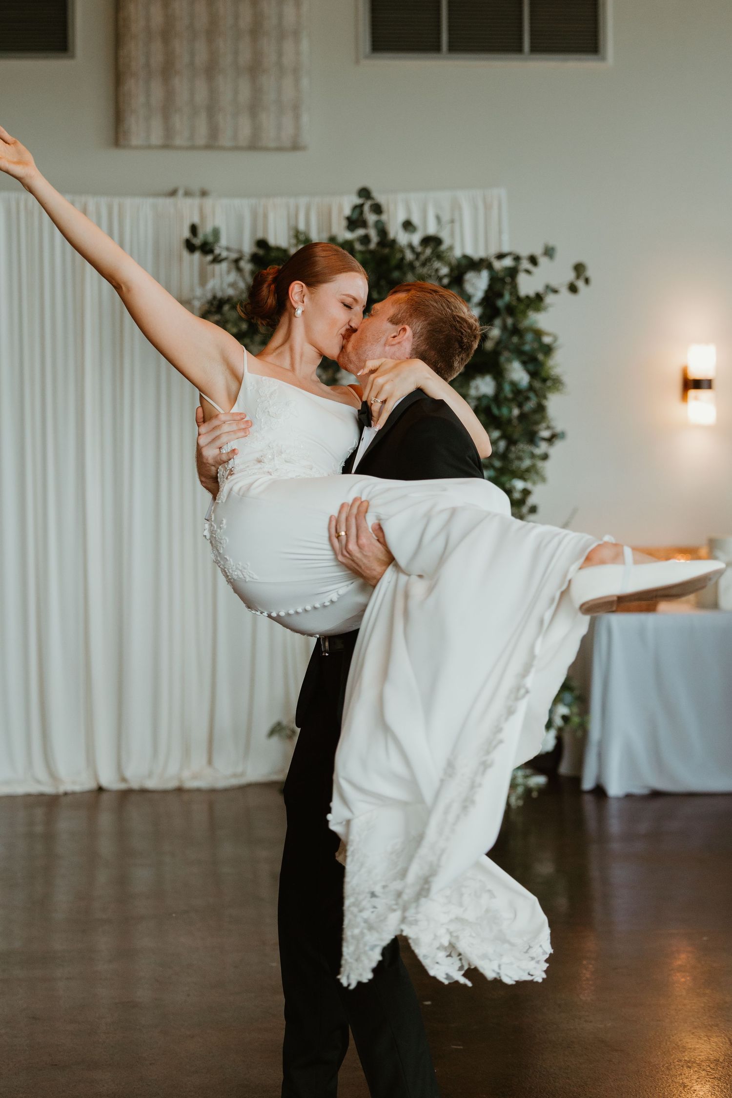 Groom lifts bride for a romantic kiss during first dance at elegant wedding reception venue.