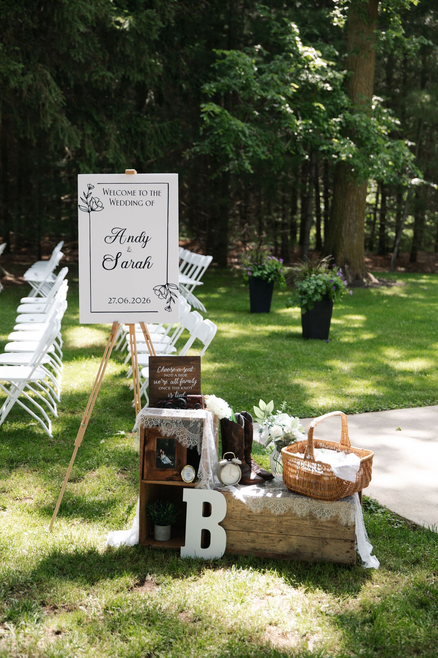 Outdoor wedding welcome sign for Andy and Sarah dated 27.06.2020 surrounded by rustic wooden decor.