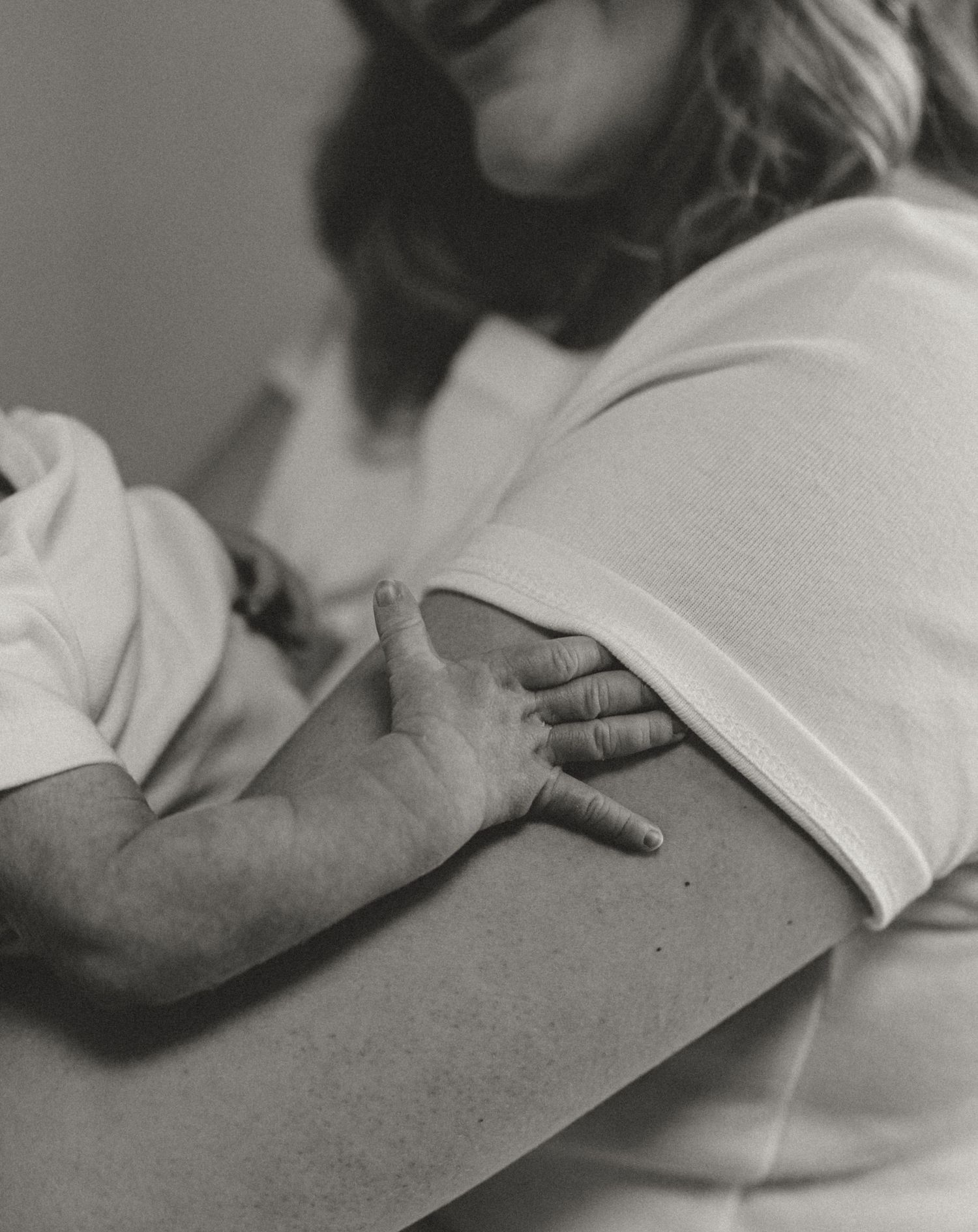 Black and white close-up of newborn baby hand resting on mothers arm.
