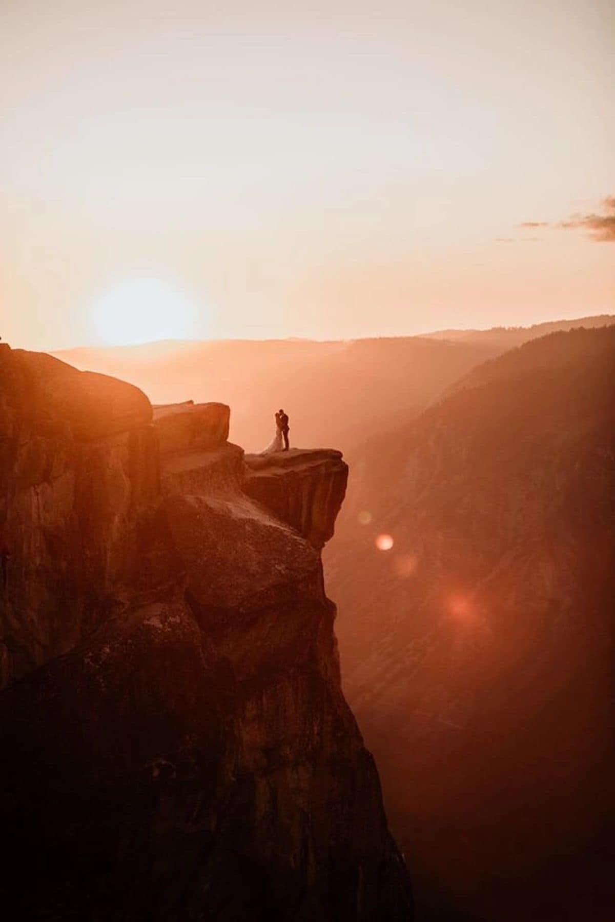 Silhouette of couple embracing on dramatic cliff edge at golden sunset in mountain canyon.