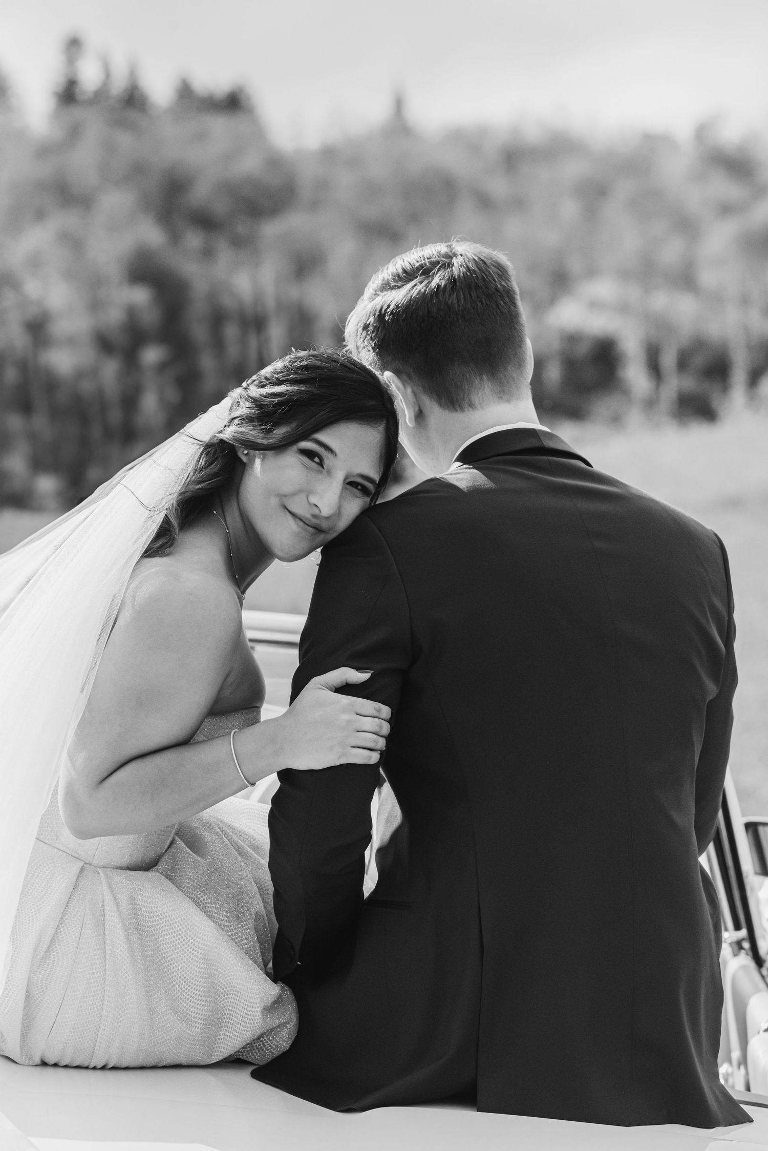 Black and white wedding photograph capturing intimate moment of bride and groom sitting outdoors.
