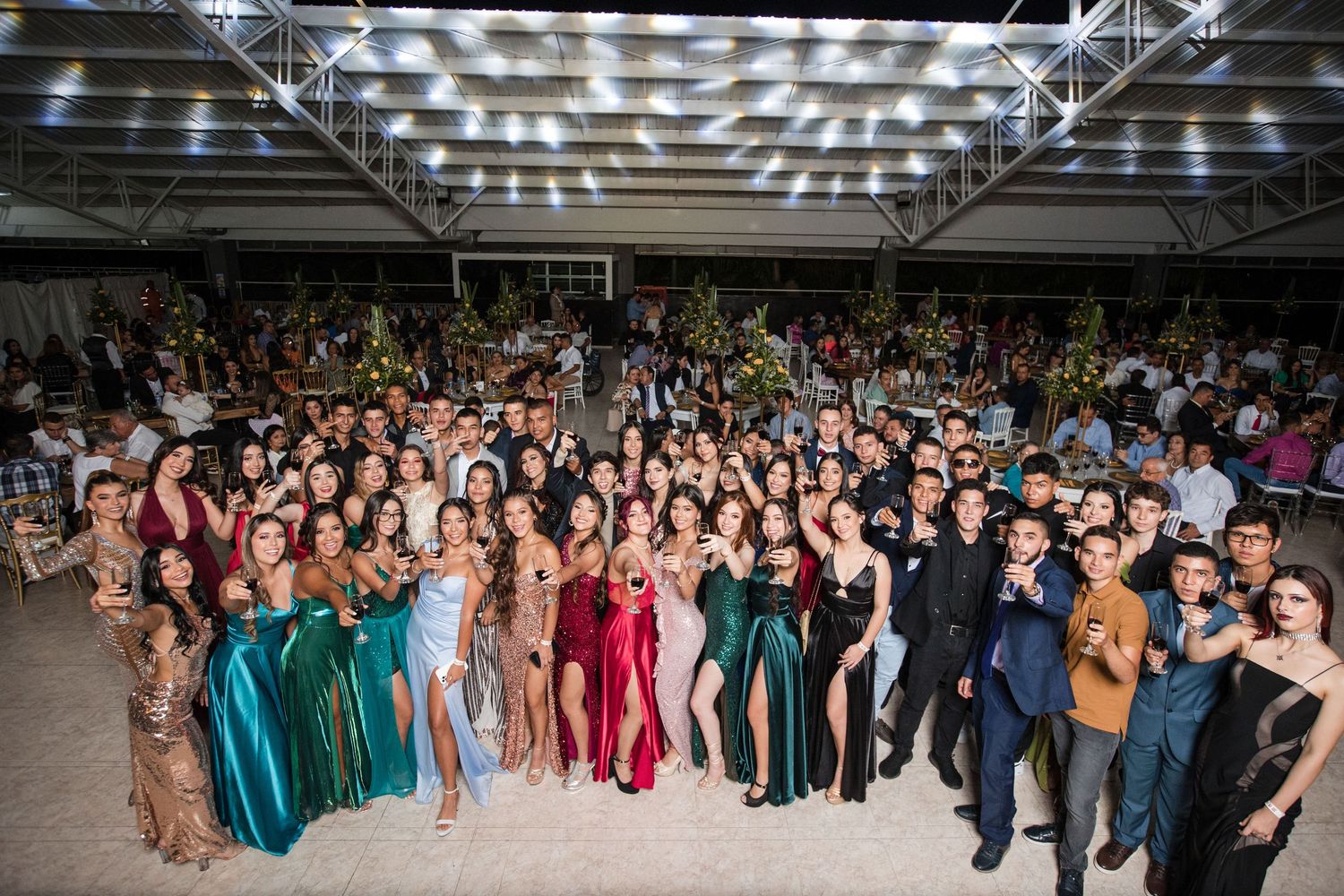 Large group photo of wedding guests and wedding party posing together at an indoor reception venue with bright lighting.