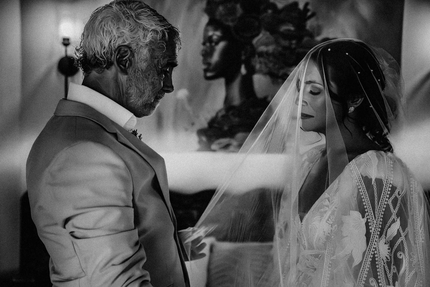 Black and white emotional wedding moment showing person in suit and bride in veil sharing tender interaction.