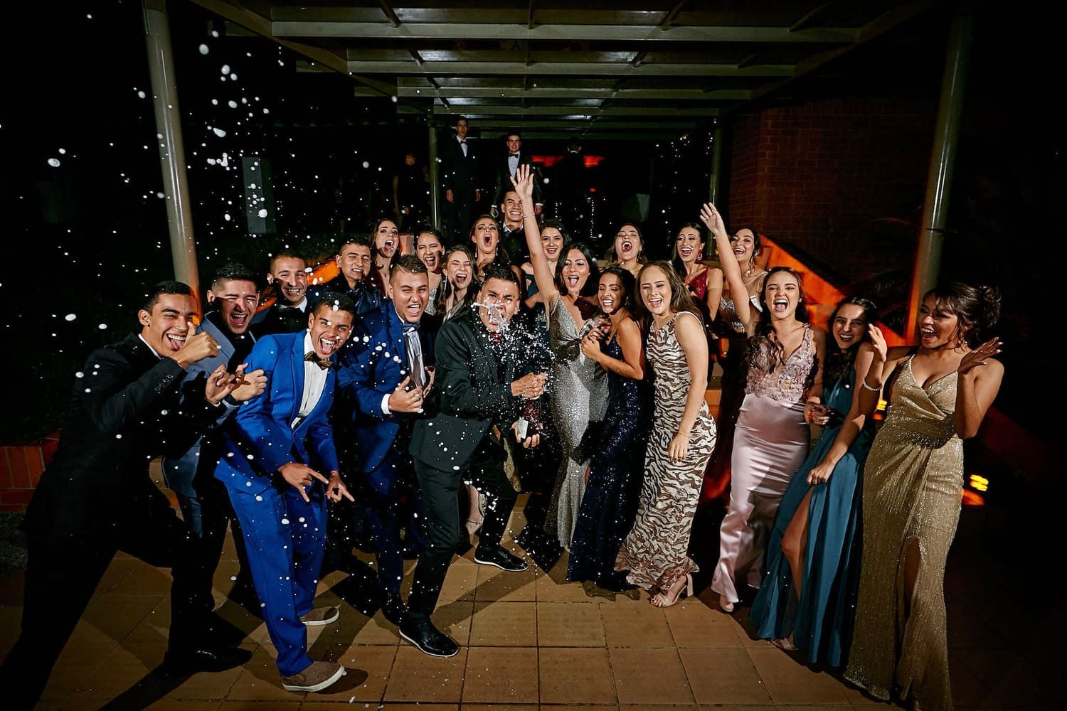 grupo de estudiantes celebrando prom de graduacion con trajes de gala y espuma en la fiesta
