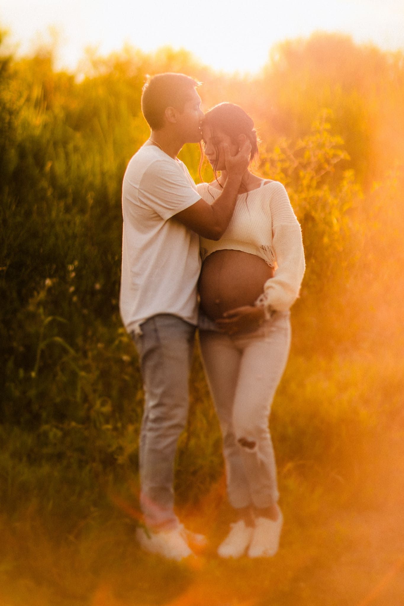 pareja abrazada en el campo al atardecer en sesion de fotos de maternidad por john palacio