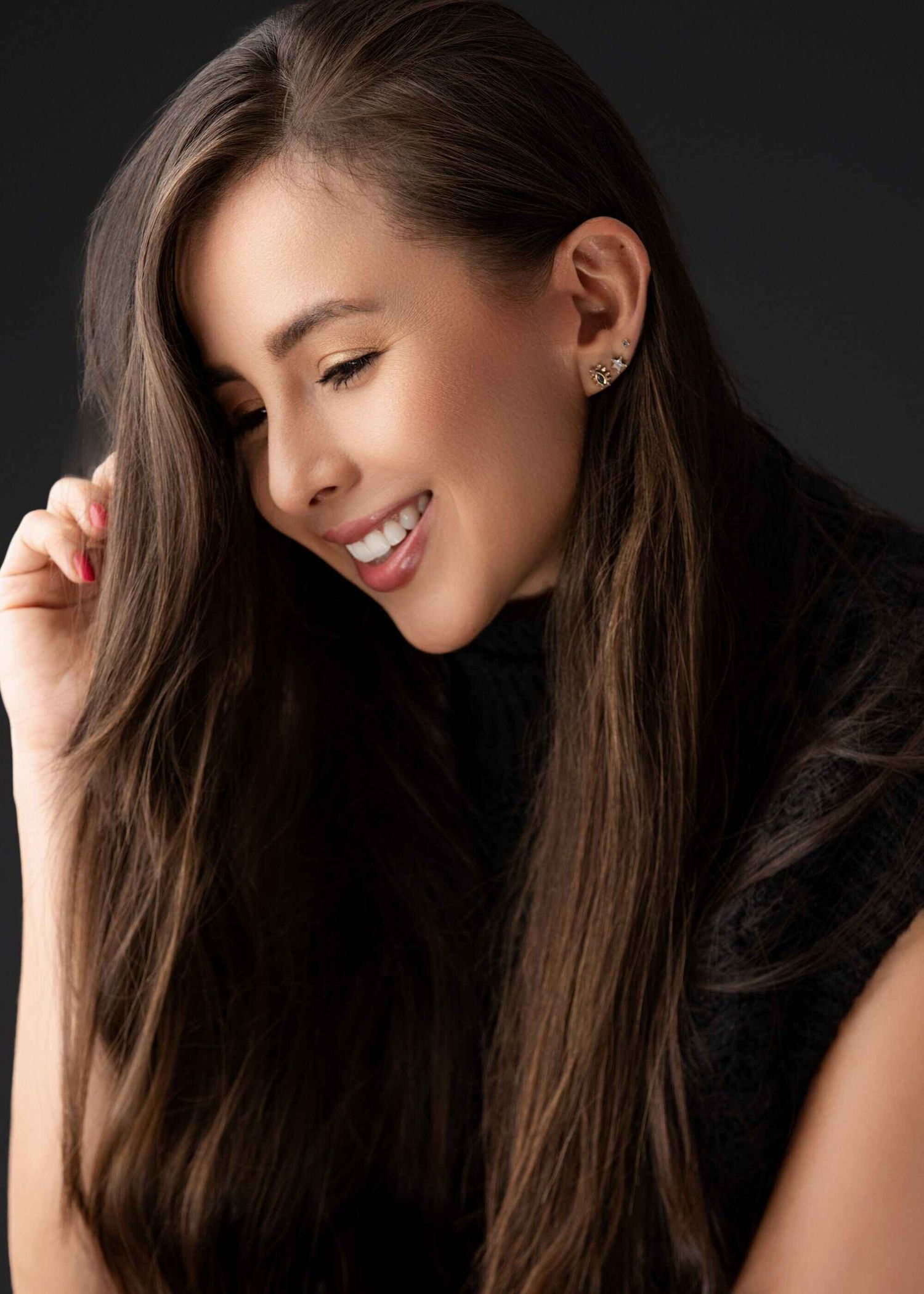 Primer plano artístico de perfil de una mujer sonriendo con cabello largo mirando hacia abajo sobre fondo negro en Pereira — John Palacio