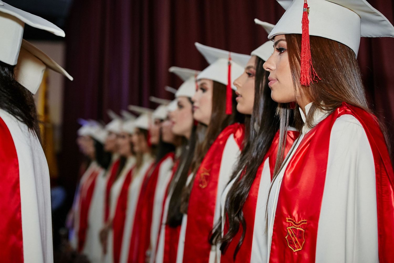 Graduates in white caps and red gowns stand in line during a formal commencement ceremony.