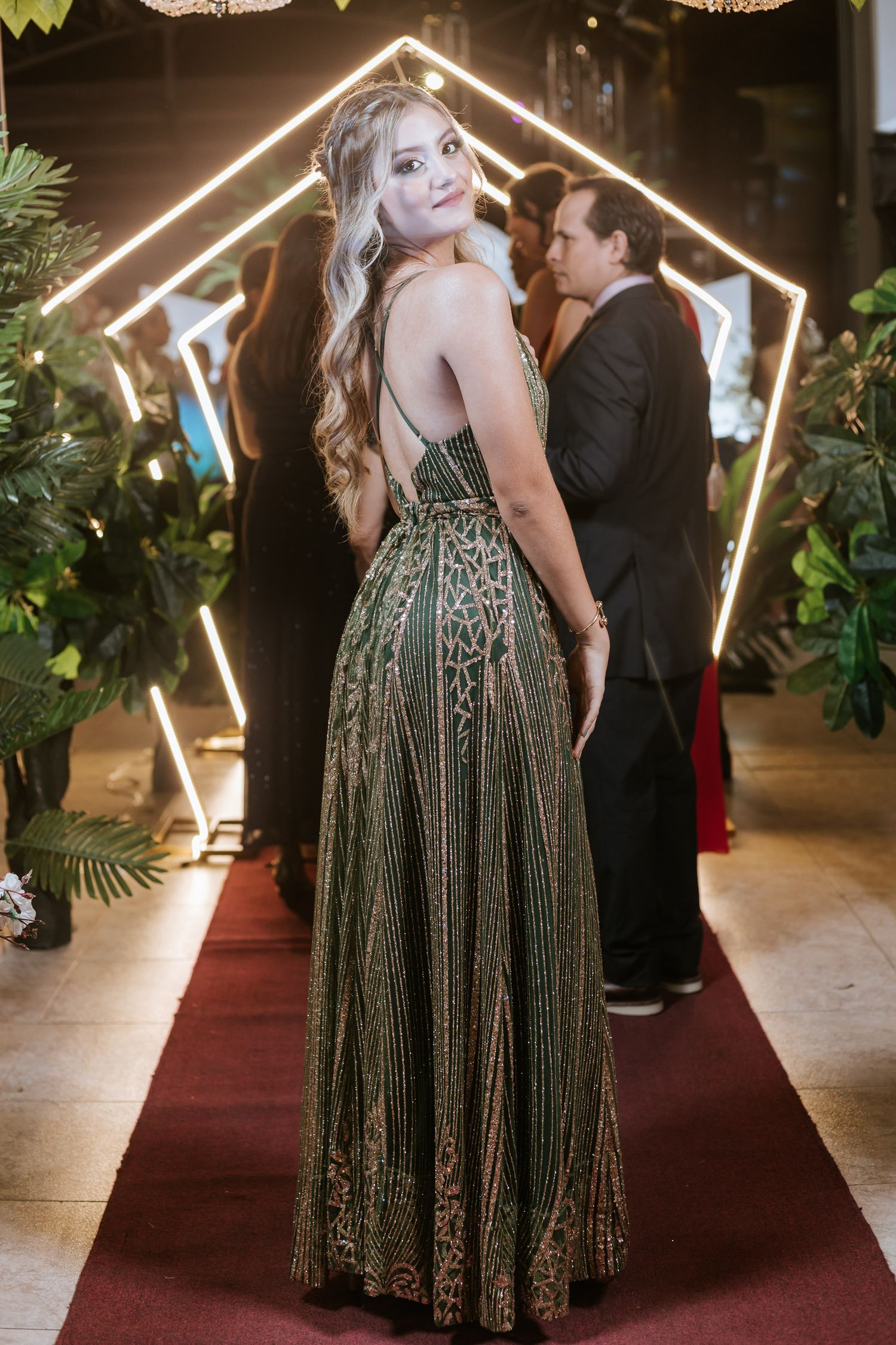 A couple dances together in front of a geometric light-up house frame display at an evening event.