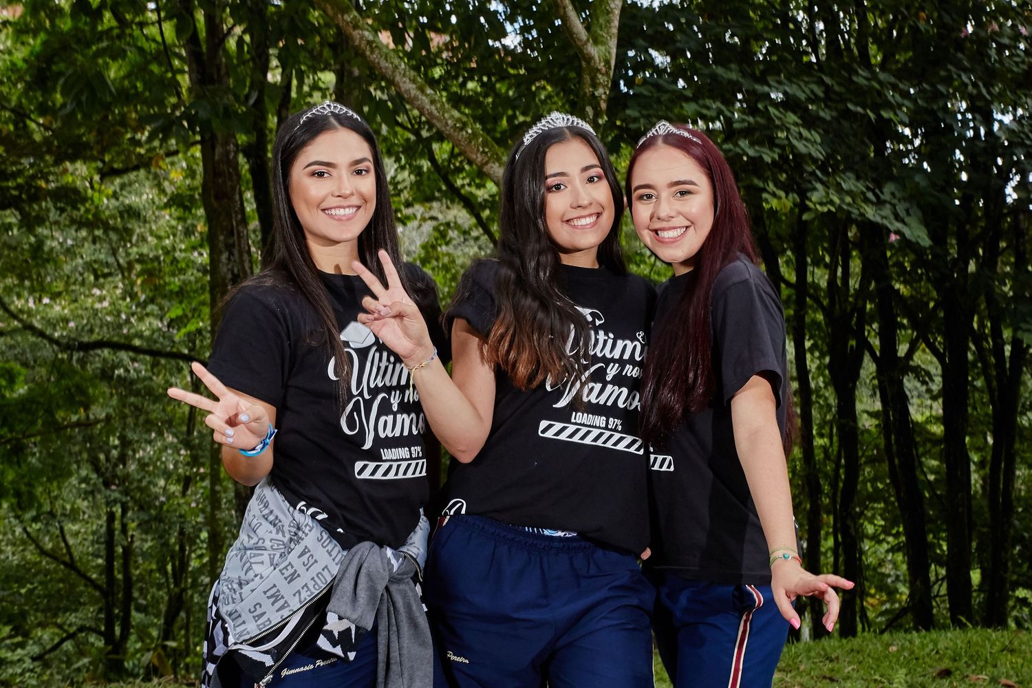 Three people wearing matching dark shirts pose together in front of trees outdoors.