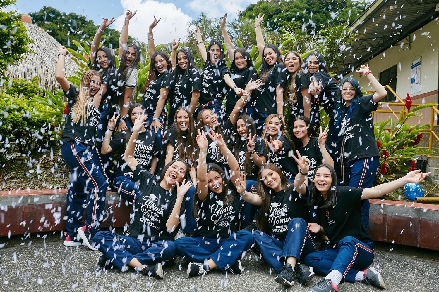 A joyful group in matching blue outfits celebrates with confetti flying in an outdoor garden setting.