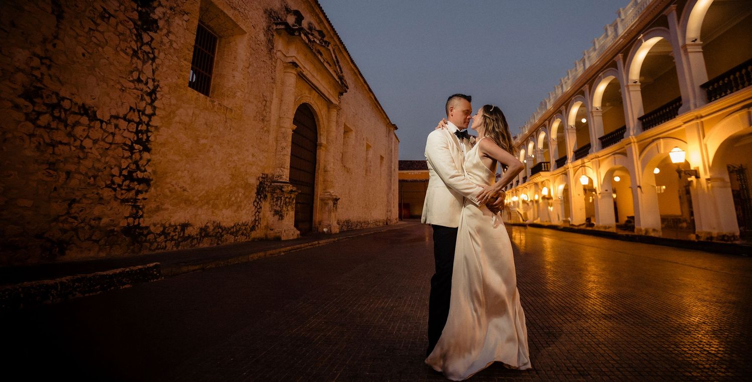 A couple embraces at night in front of illuminated colonial arches at Antigua Guatemala's historic ruins.