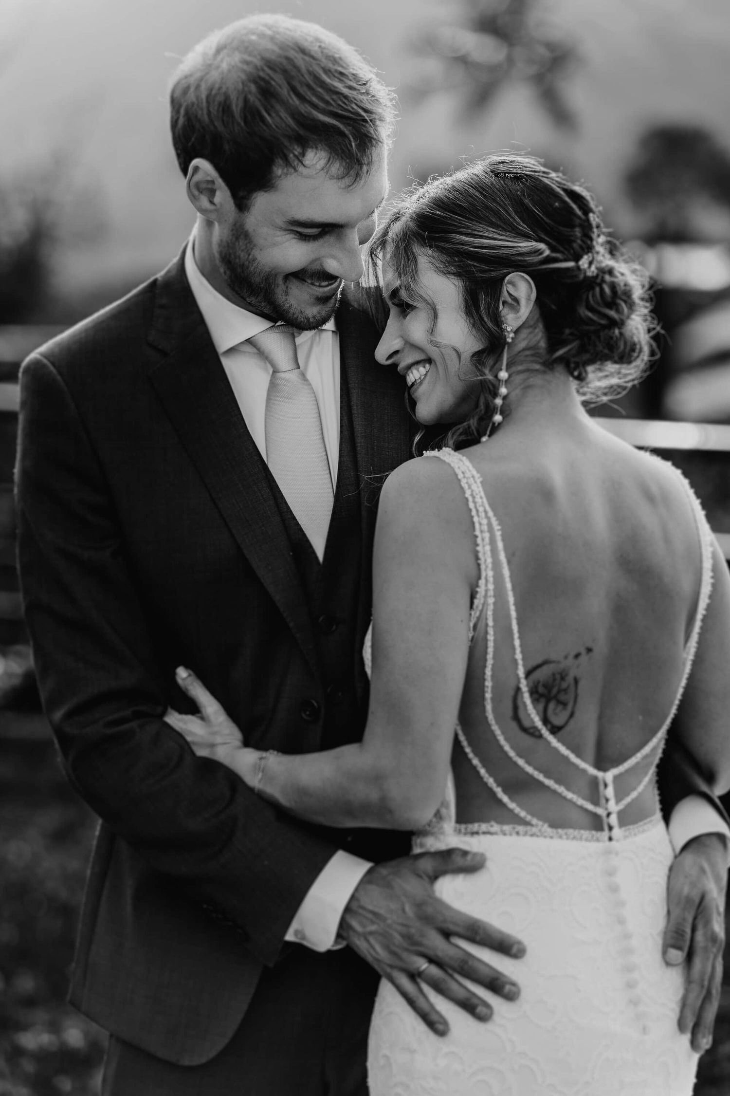 Black and white wedding photo showing a joyful couple sharing an intimate moment outdoors in formal attire.