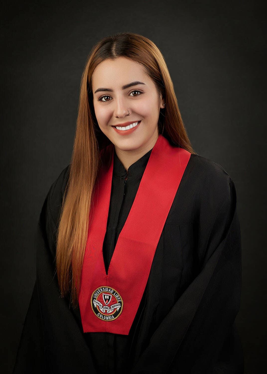 Professional graduation portrait featuring a student wearing a black gown with red sash and university emblem.