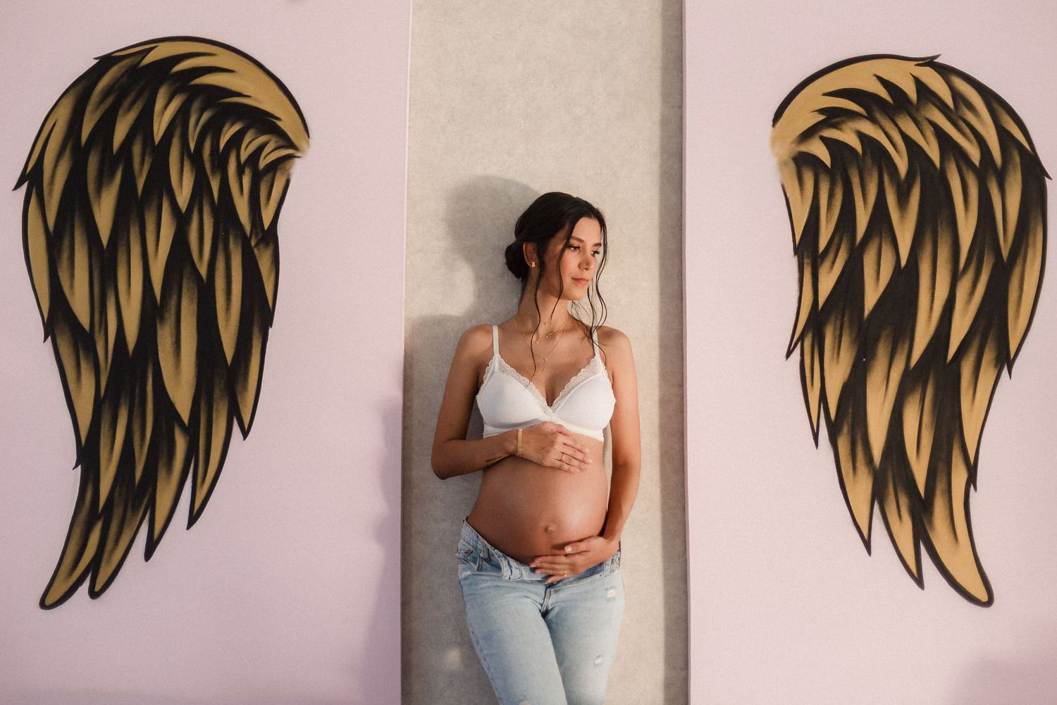 mujer embarazada posando con alas de angel pintadas en estudio para sesion de fotos de embarazo