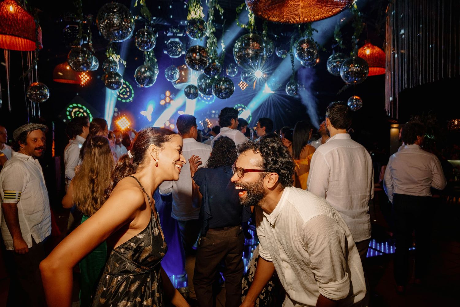 Pareja riendo y bailando juntos durante la celebración de boda con luces y bolas de espejo.