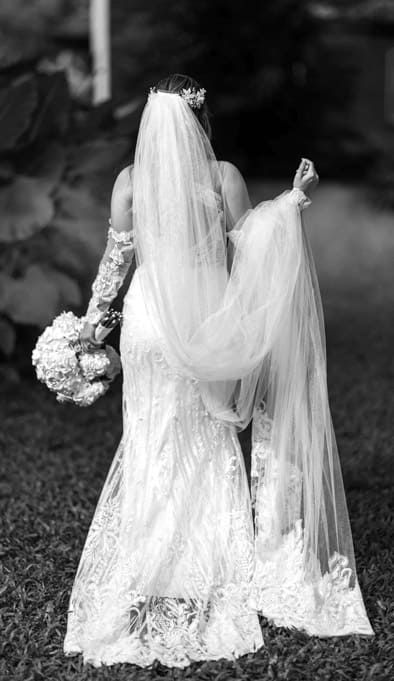 Cartagena wedding photographer capturing bride from the back with long veil and bouquet, black and white garden portrait