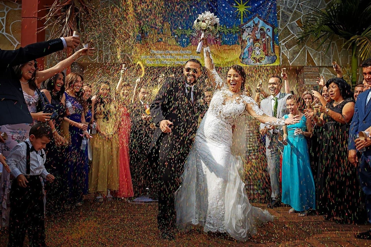 Novios celebrando sonrientes con lluvia de confeti y familia tras ceremonia de matrimonio.