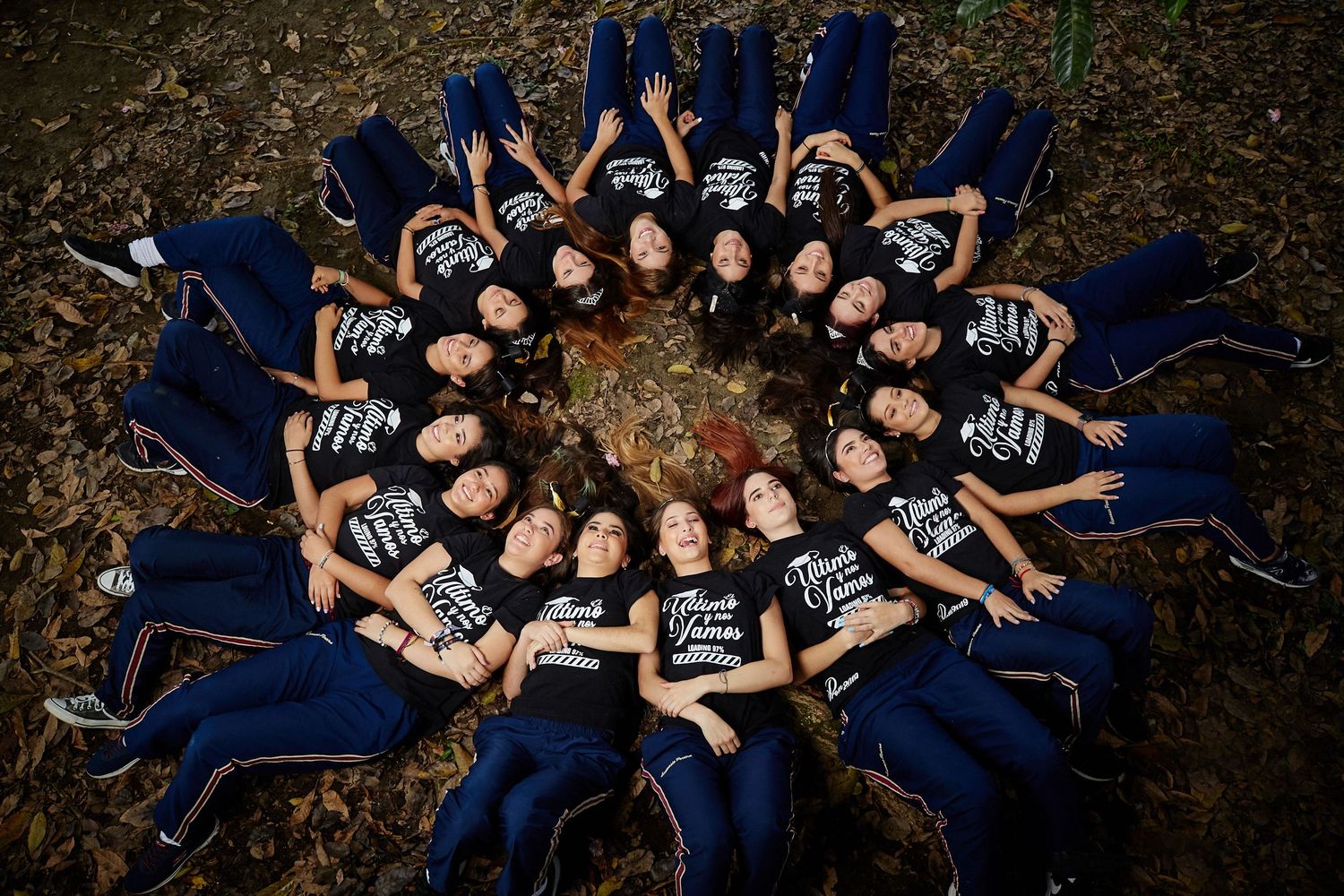 People wearing navy blue outfits lay in a circle formation on autumn leaves creating an artistic aerial view pattern.
