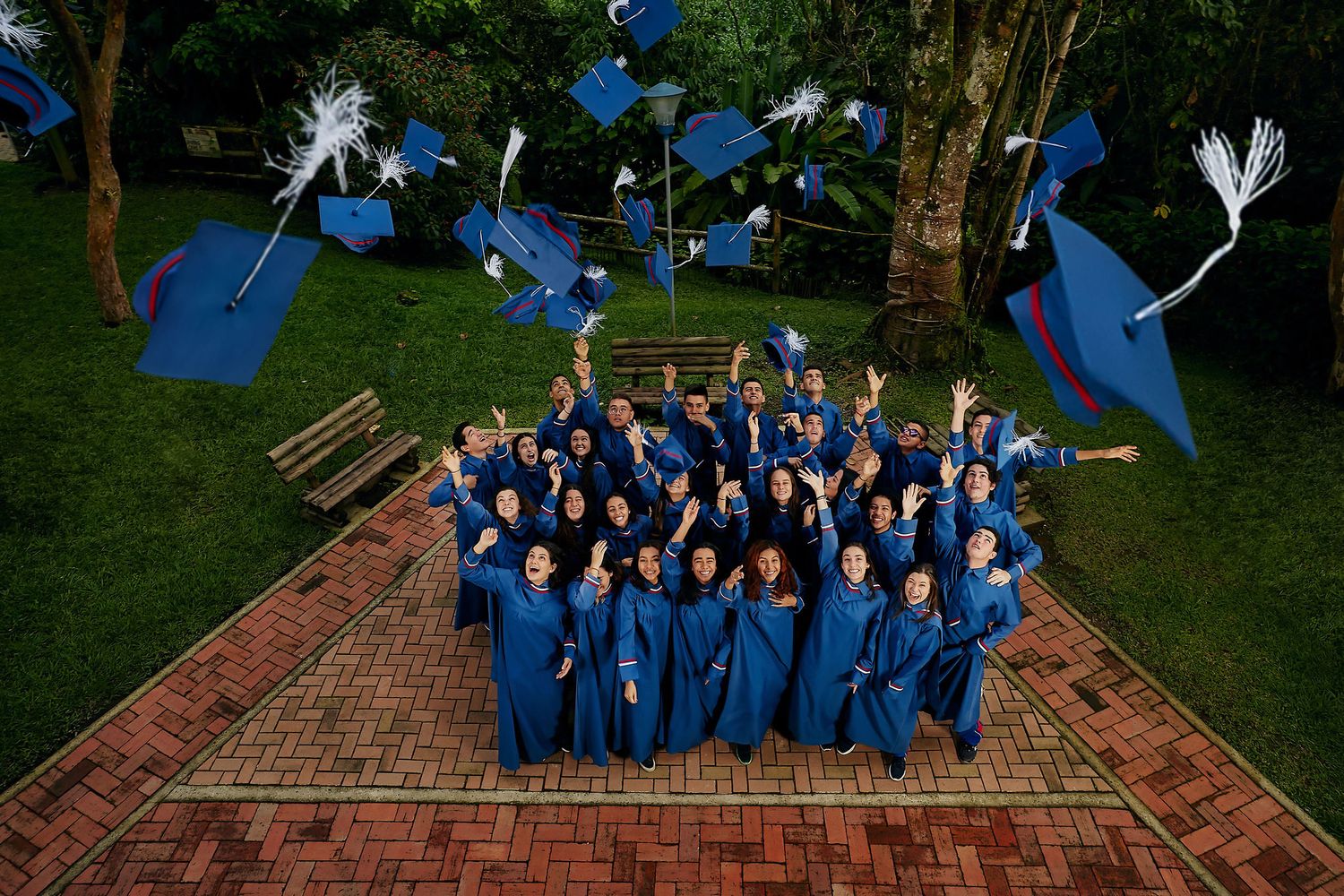 Graduates in blue caps and gowns pose together on a brick pathway in a garden setting.