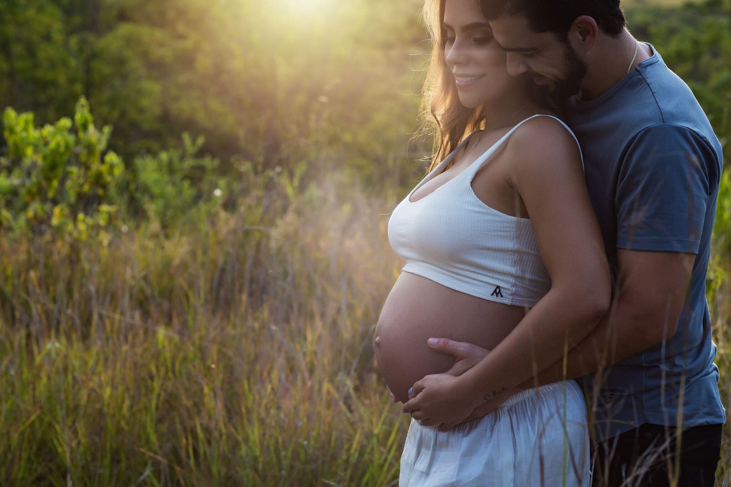 pareja abrazada mostrando barriga en sesion de fotos de embarazo al atardecer