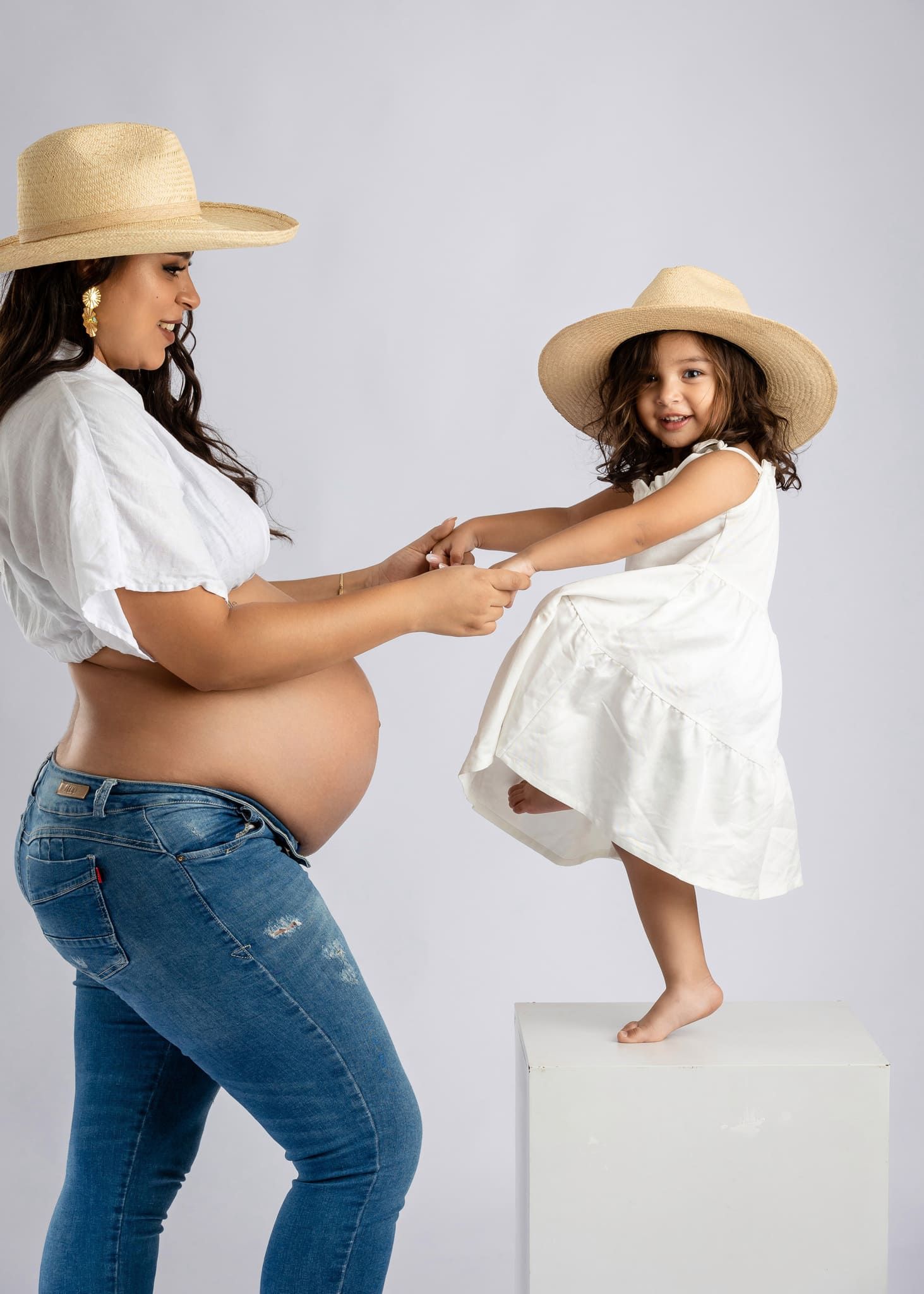 mujer embarazada vestida de blanco sentada en el pasto mirando su barriga en sesion de fotos de maternidad por john palacio
