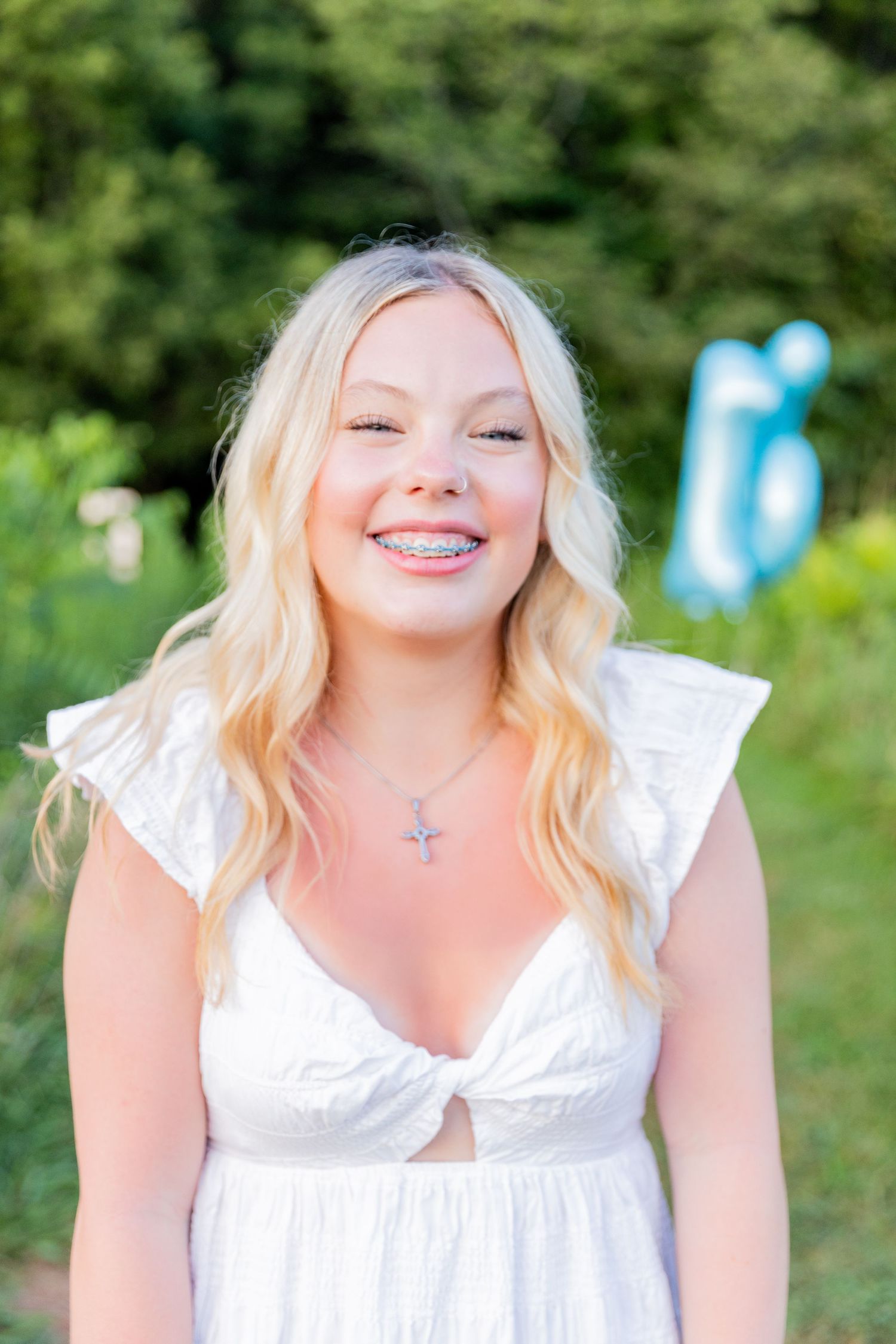 Candid summer photoshoot with white dress and blue balloons in a wooded background.