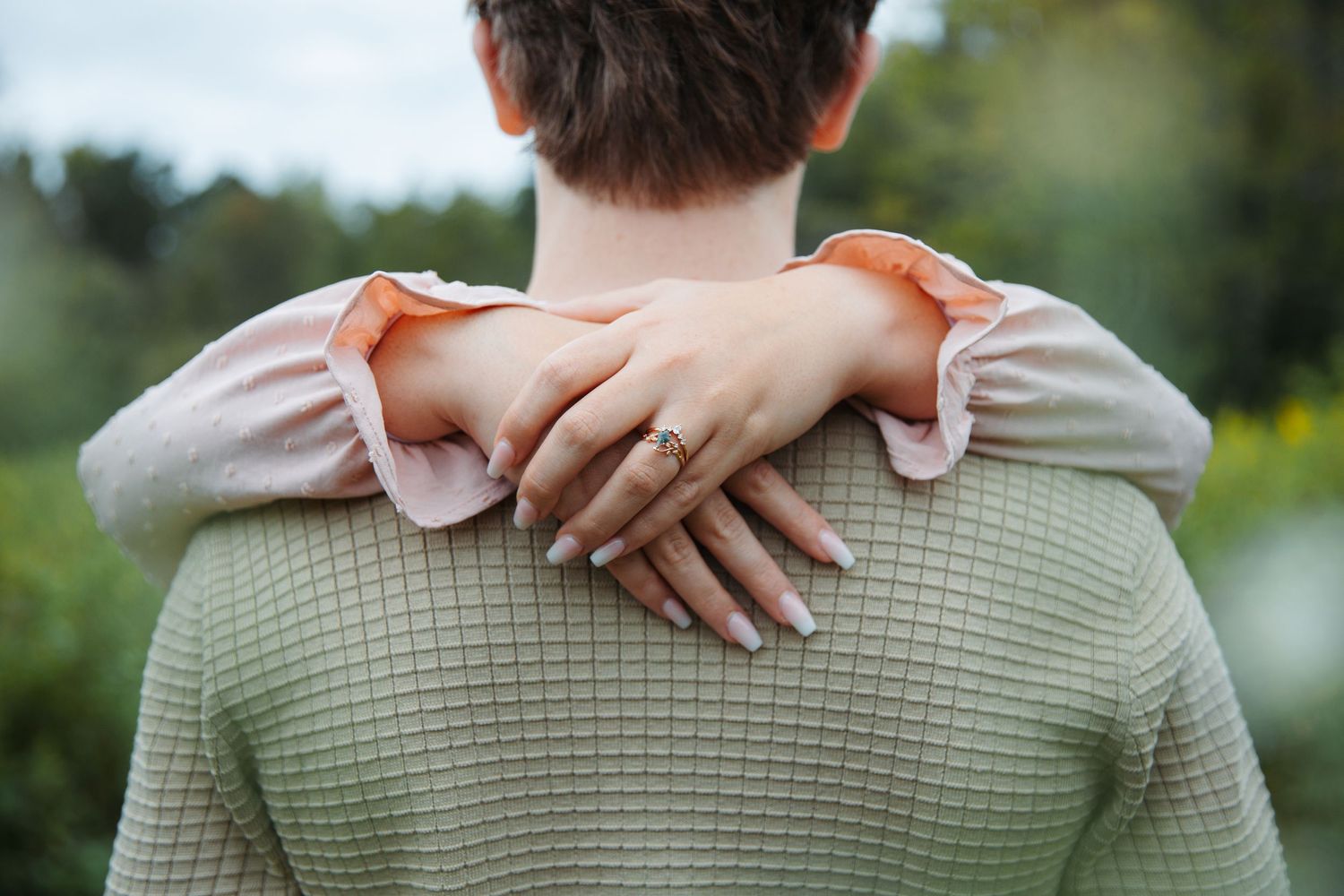 Close-up detail of hands resting on a textured green sweater showing engagement ring.